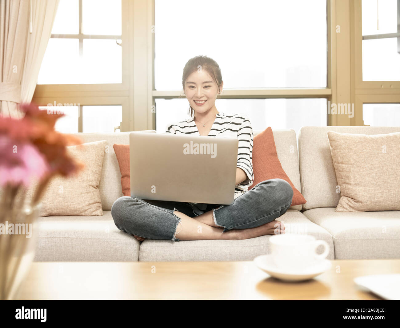 Bella e felice giovane donna asiatica di lavoro a casa sittng sul lettino usando il computer portatile Foto Stock