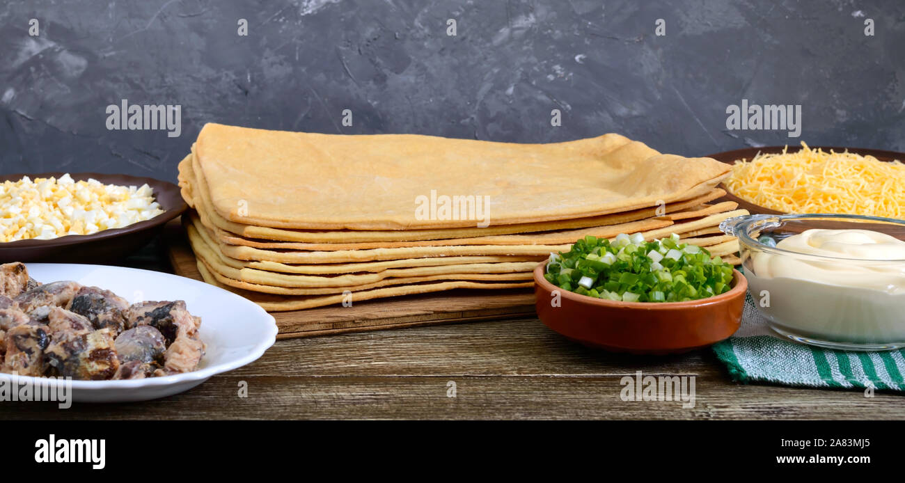 Ingredienti per la produzione di uno snack dolce di sfoglia di uova, formaggio, erbe, conserve di pesce, la maionese su un tavolo di legno. Foto Stock