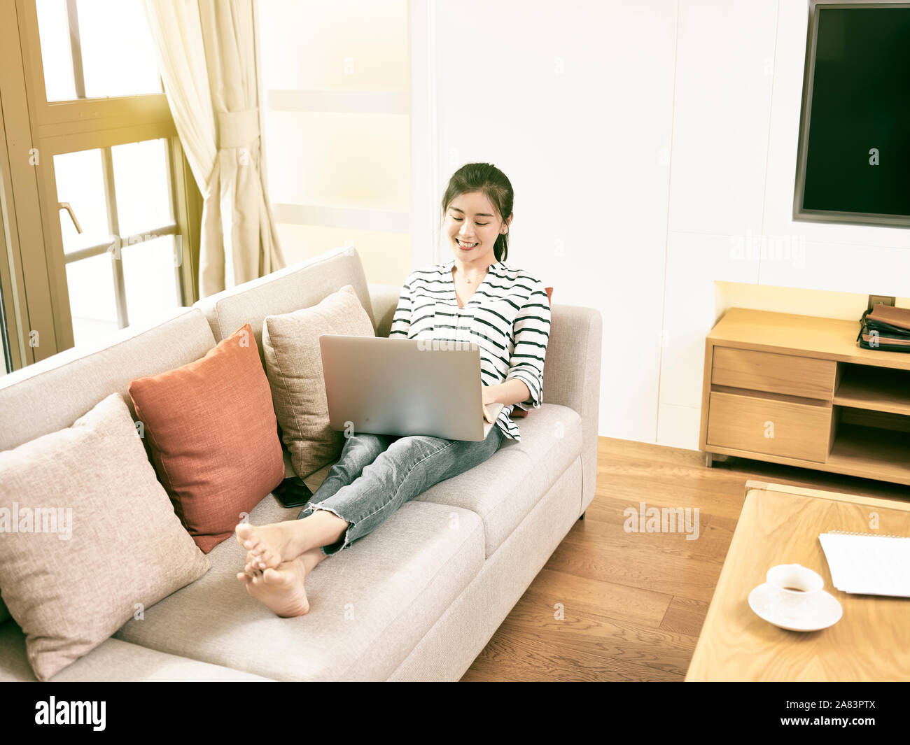 Bella e felice giovane donna asiatica di lavoro a casa sittng sul lettino usando il computer portatile, ad alto angolo di visione Foto Stock