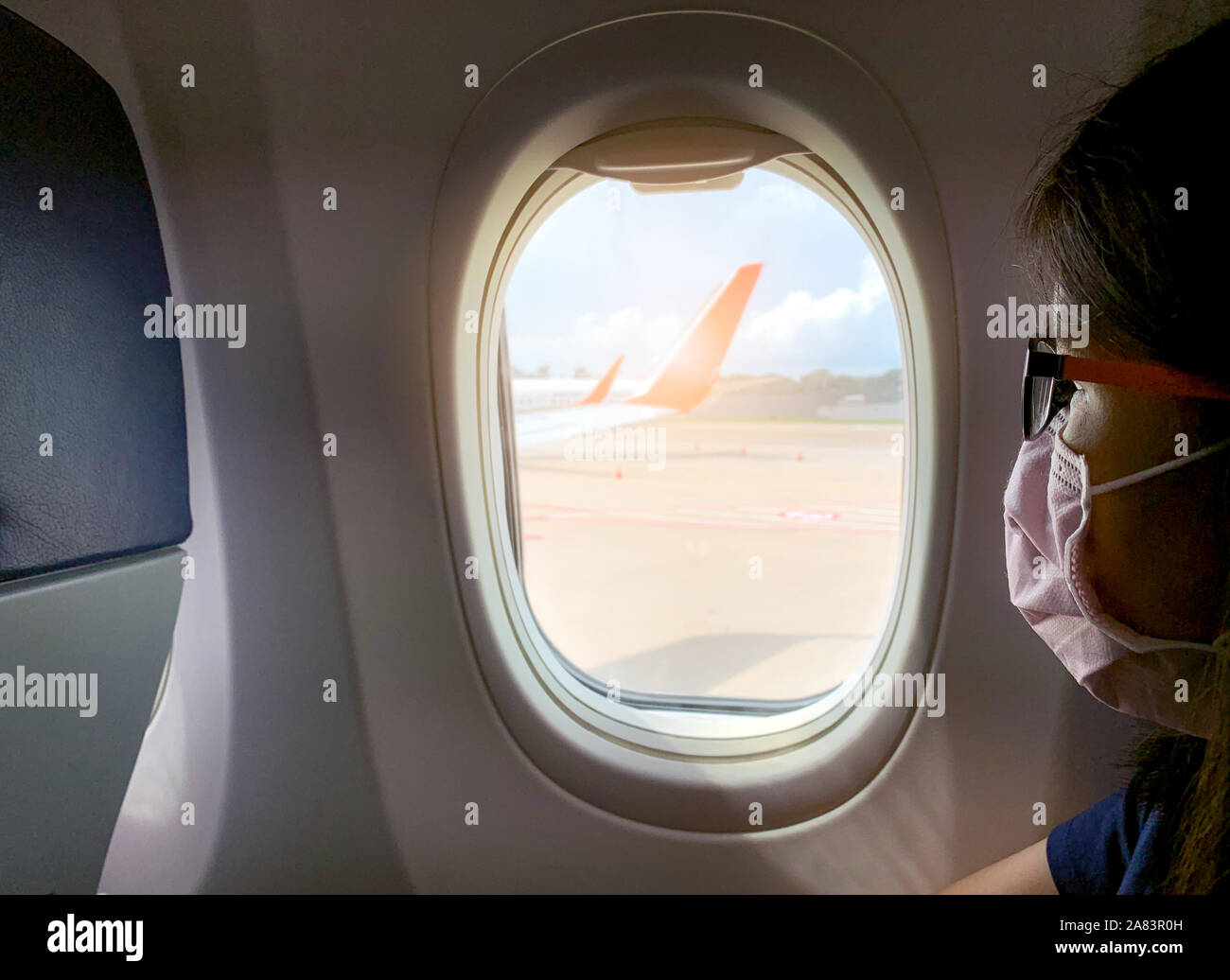 Malata passeggero indossare la maschera per il viso e occhiali sedersi sulla economia passeggero sedile vicino al finestrino della cabina all'interno del velivolo. Passeggero in partenza piano di volo Foto Stock