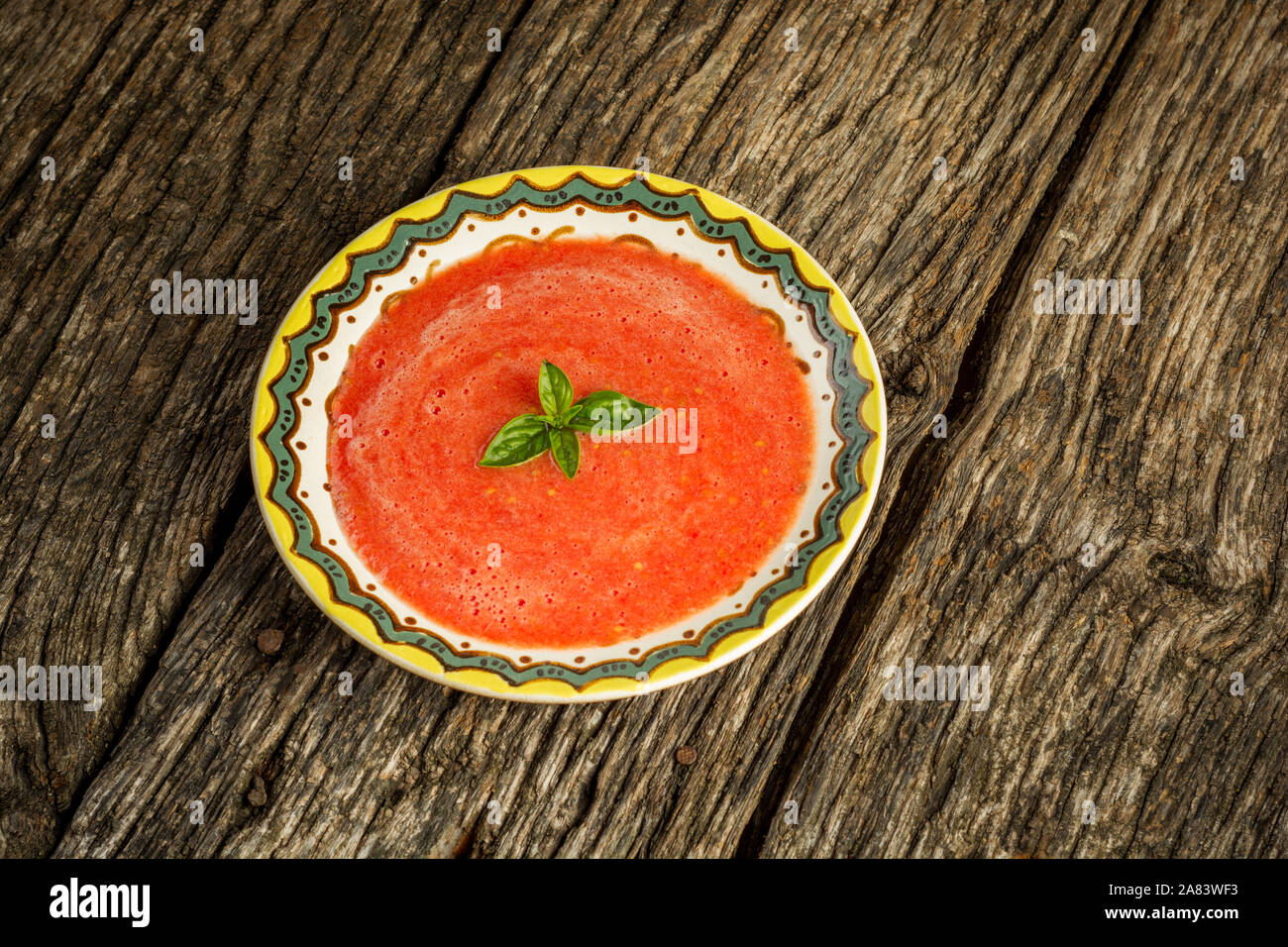 Zuppa Gazpacho con il verde del basilico in vaschetta di colore giallo su sfondo rustico. Spagnolo tradizionale zuppa fredda purea. Foto Stock