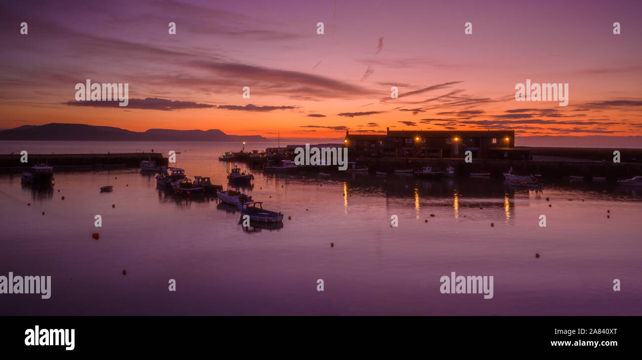 Lyme Regis, Dorset, Regno Unito. Il 6 novembre 2019. Regno Unito Meteo: bellissima alba presso il centro storico di Porto di Cobb nella località costiera comune di Lyme Regis. Barche ormeggiate nel porto profilarsi come il cielo si illumina con morbide tonalità rosa su una fredda mattina davanti a turbate condizioni meteo più tardi. Credito: Celia McMahon/Alamy Live News. Foto Stock