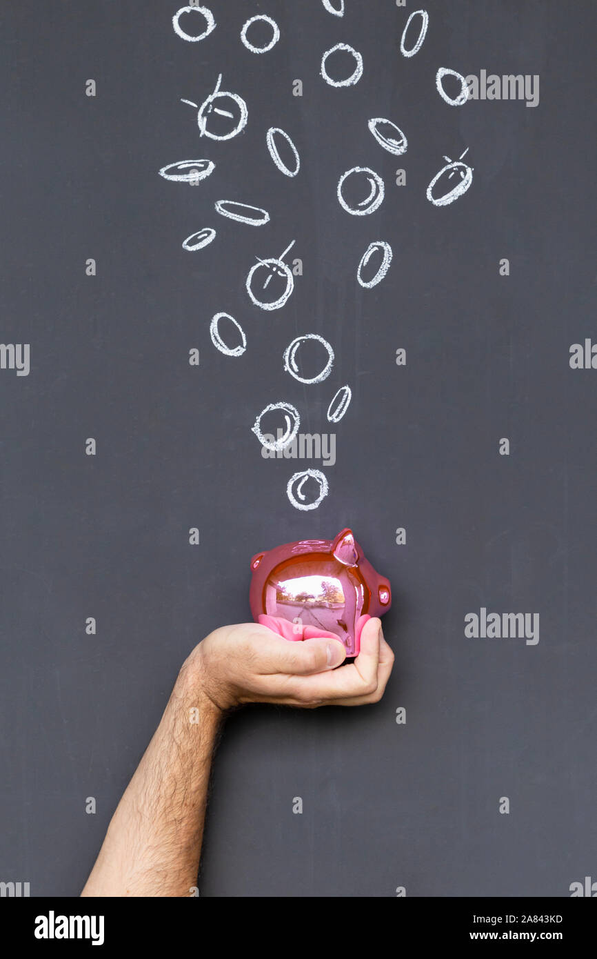 Concetto di risparmio di denaro con una colorazione rosa salvadanaio tenuto in una mano di fronte a una lavagna con disegnati a mano delle monete in euro Foto Stock