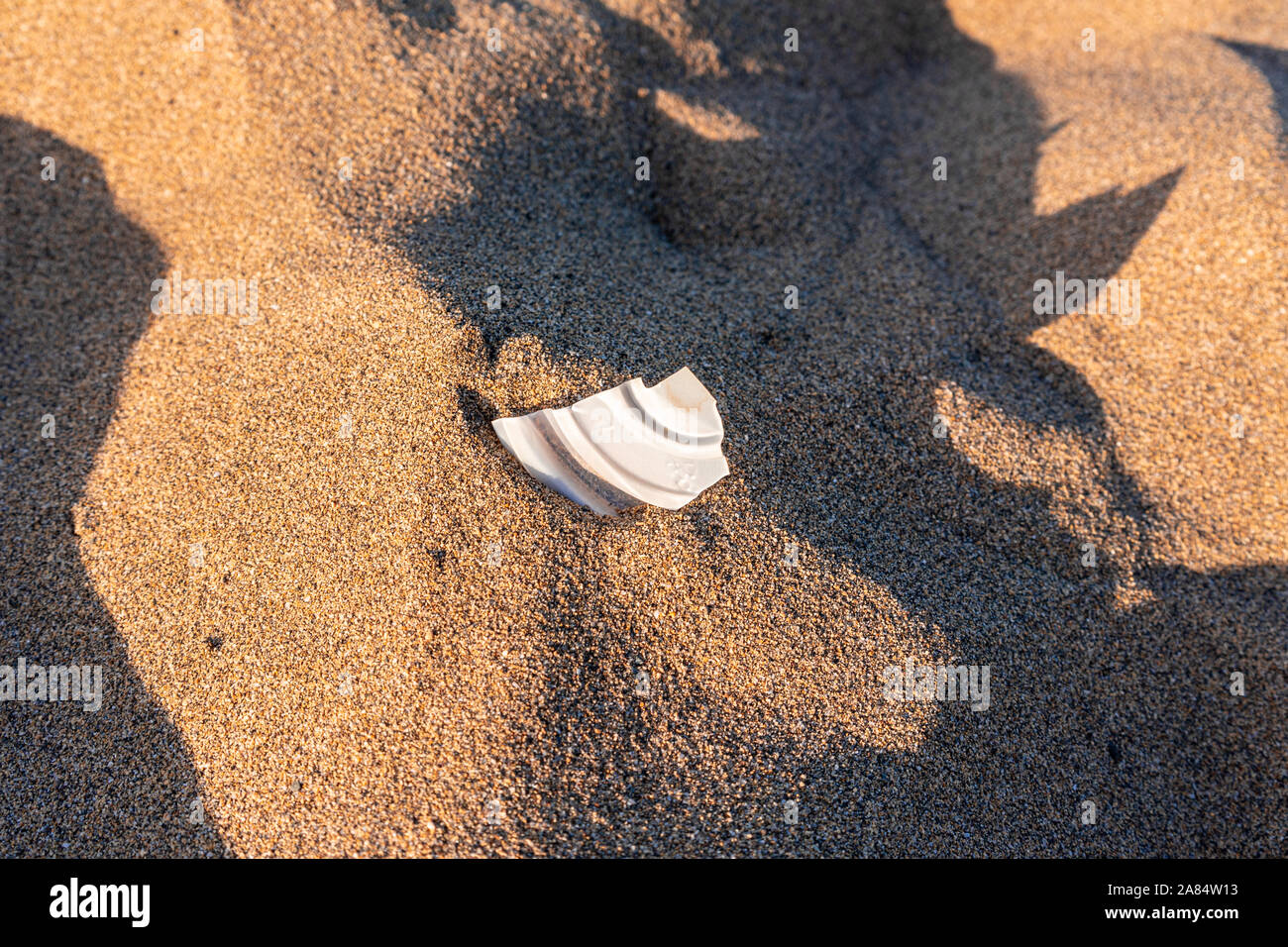 Piccolo pezzo di plastica bianca incorporato nella sabbia di una spiaggia Foto Stock