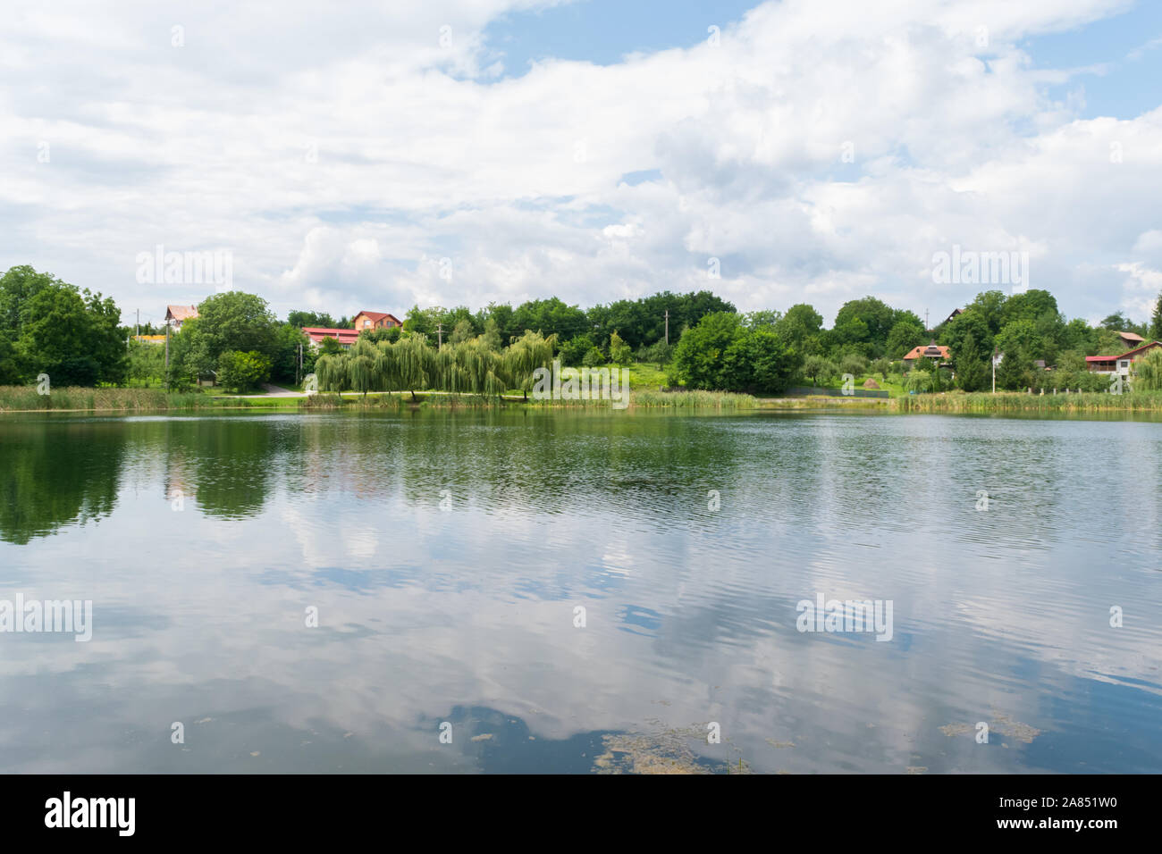 Lago calmo con vegetazione verde e case in background Foto Stock