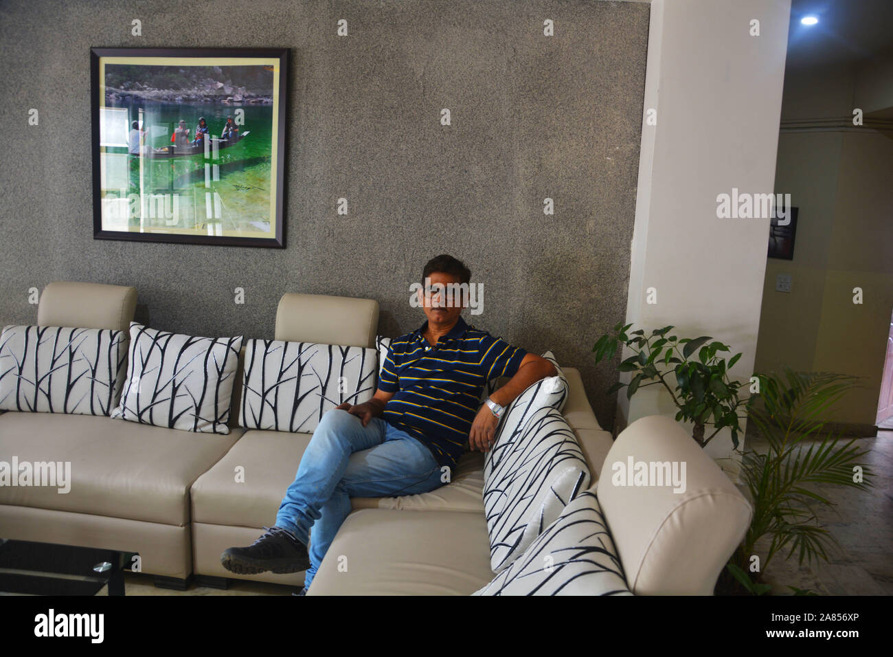 Uomo seduto su un divano con cuscini rilassanti e una fotografia appesa a una parete Foto Stock