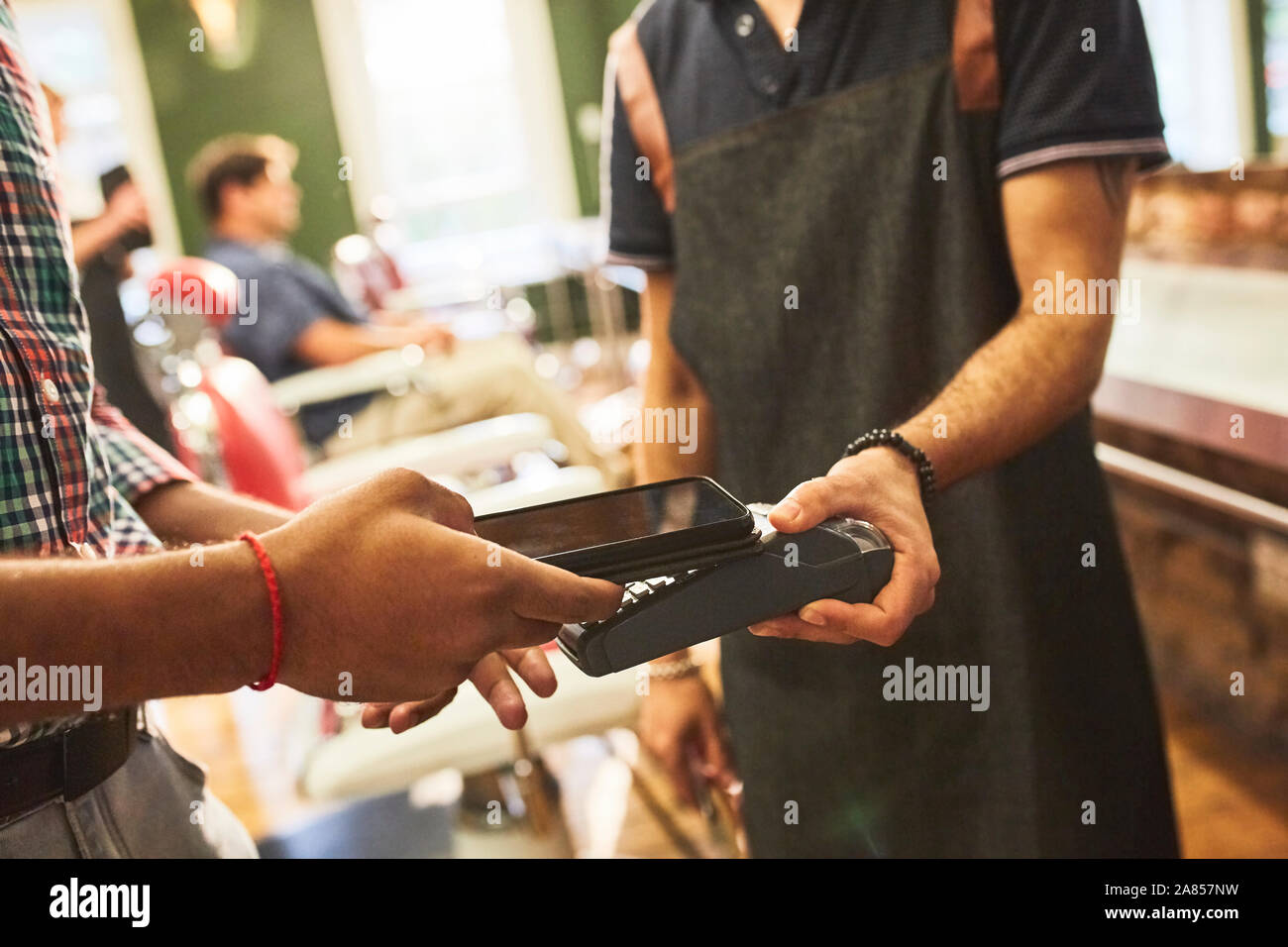 Cliente maschio prestando barbiere con smart phone il pagamento senza contatto in Barberia Foto Stock