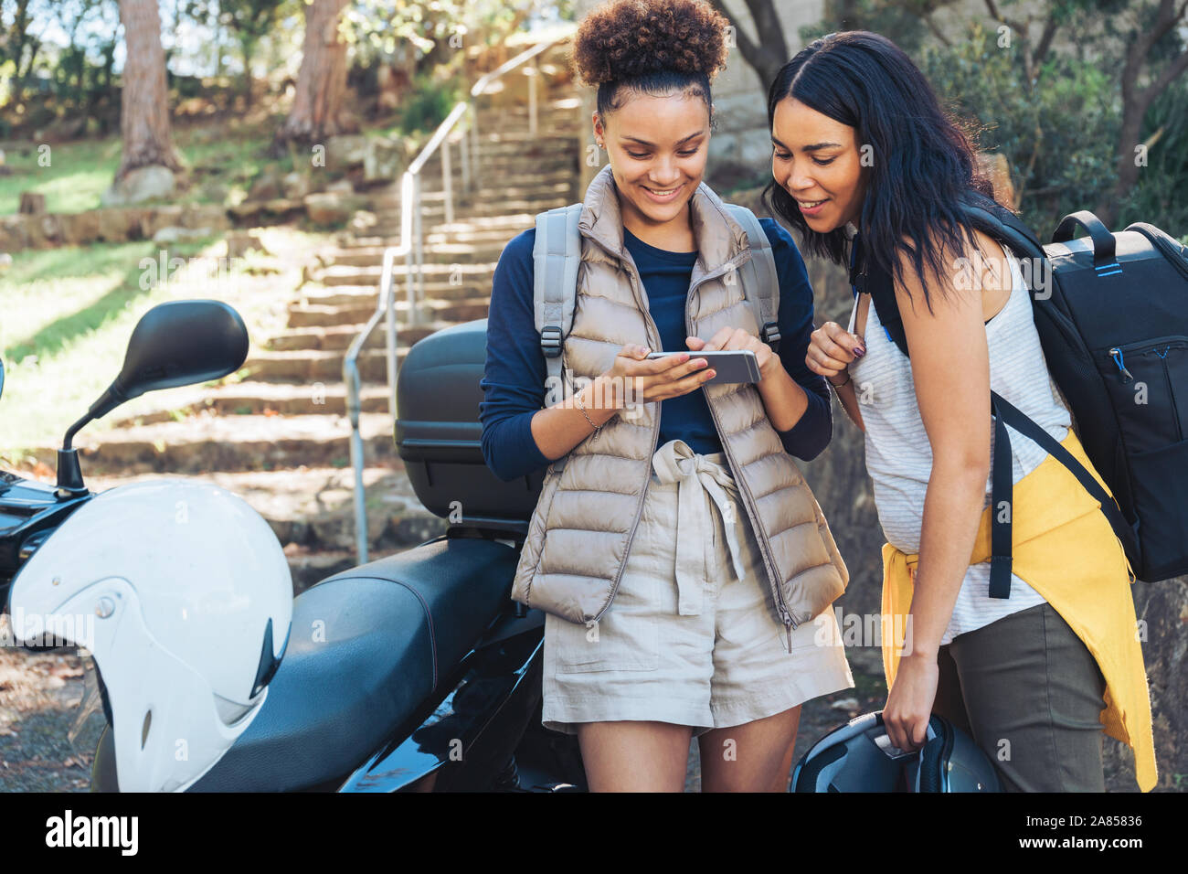 Giovani donne amici utilizzando smart phone in scooter Foto Stock