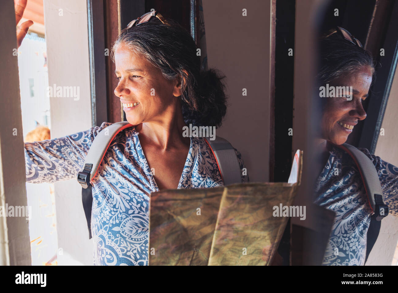 Sorridente turista femminile con mappa a guardare fuori dalla finestra di sole Foto Stock