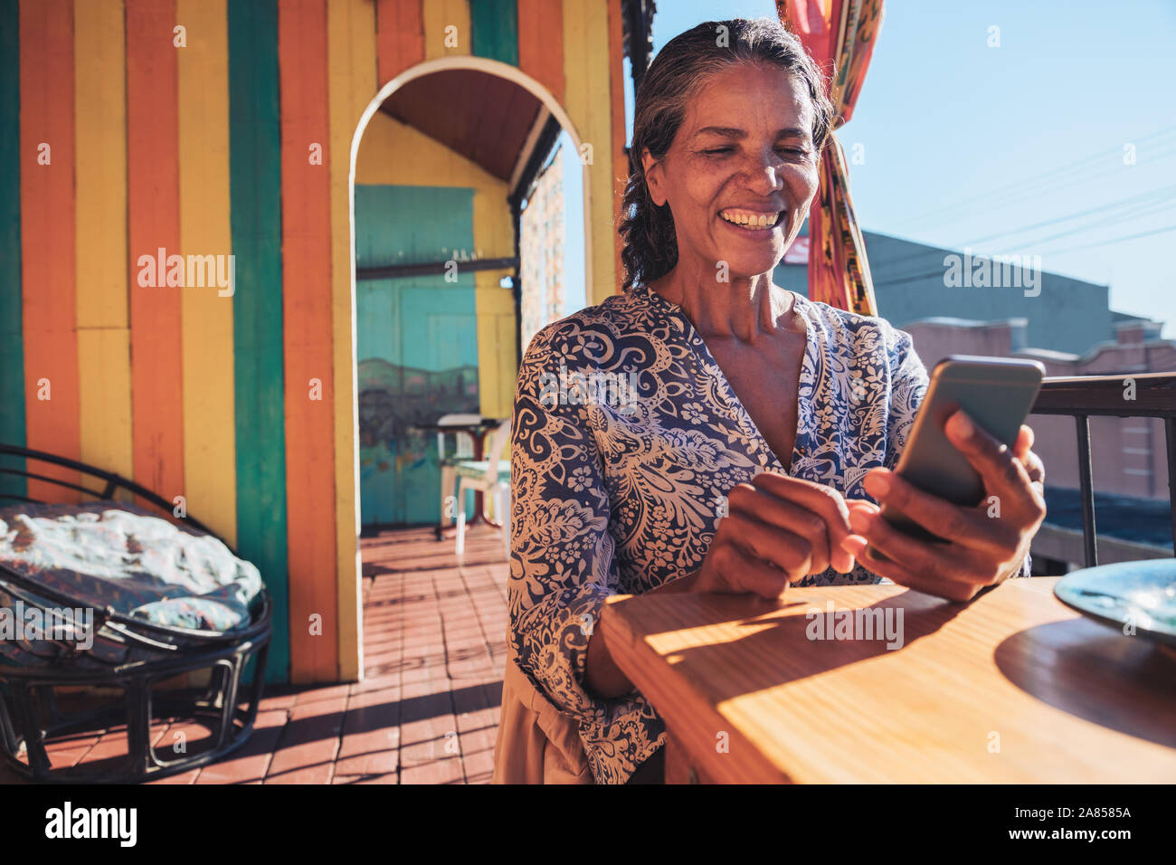 Sorridente, donna felice utilizzando smart phone sul soleggiato balcone ristorante Foto Stock