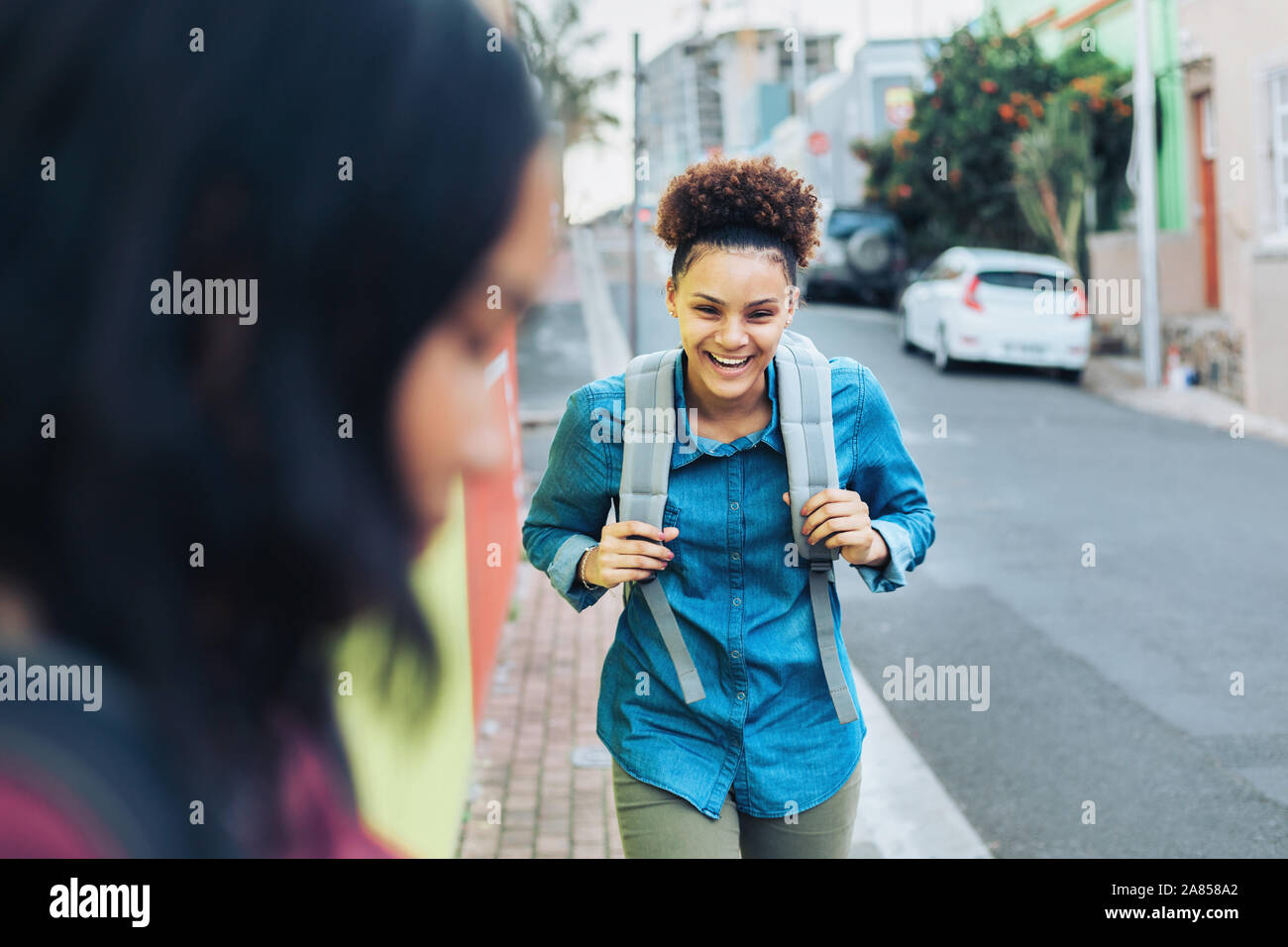 Ridendo, felice giovane donna con zaino sul marciapiede Foto Stock