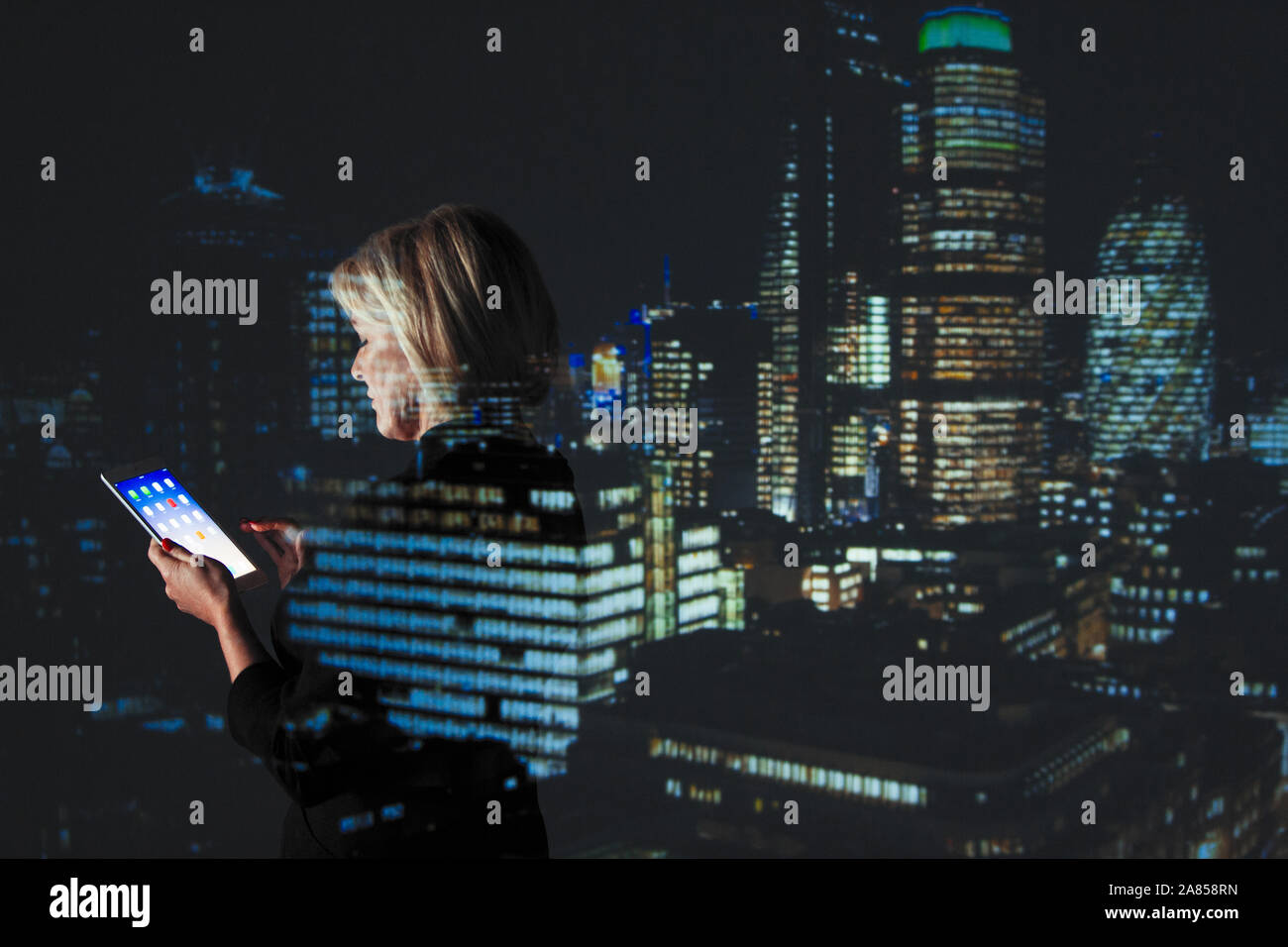 La doppia esposizione imprenditrice utilizzando digitale compressa contro il grattacielo luci di notte Foto Stock