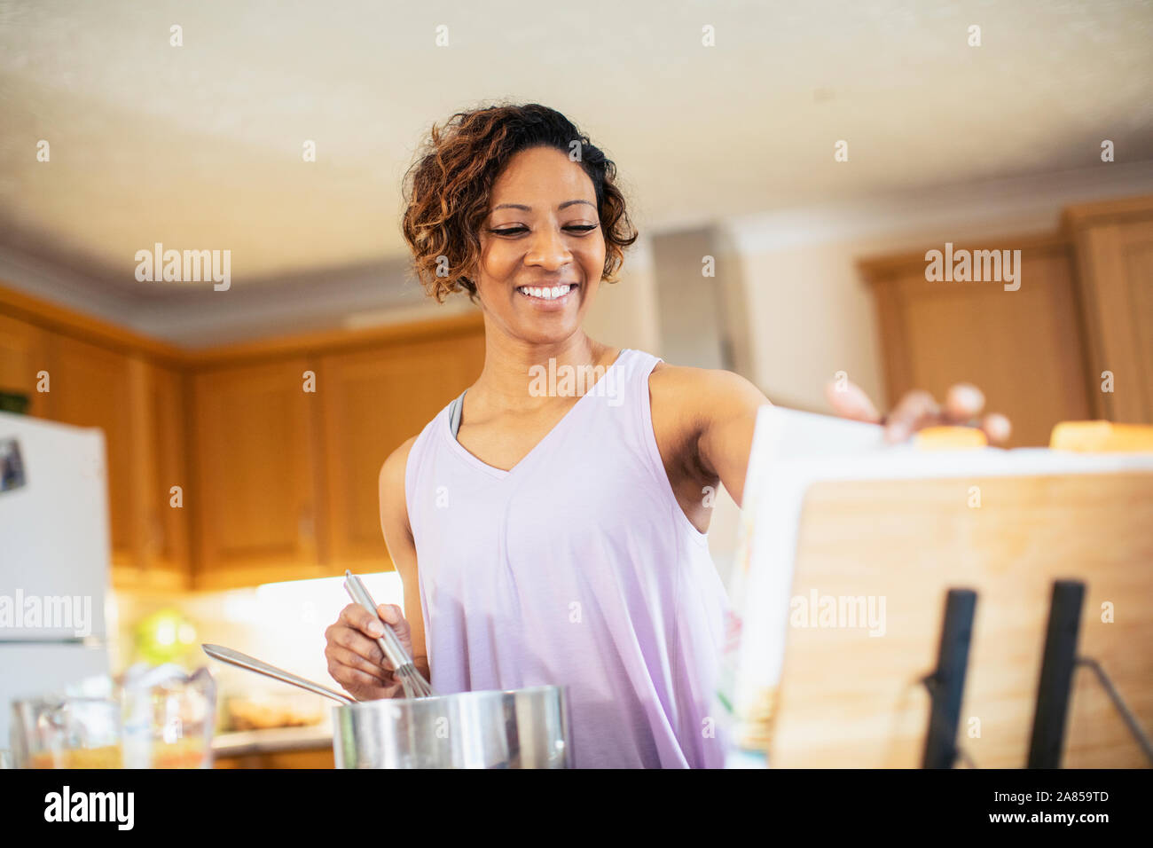 Donna sorridente con il libro di cucina in cucina Foto Stock