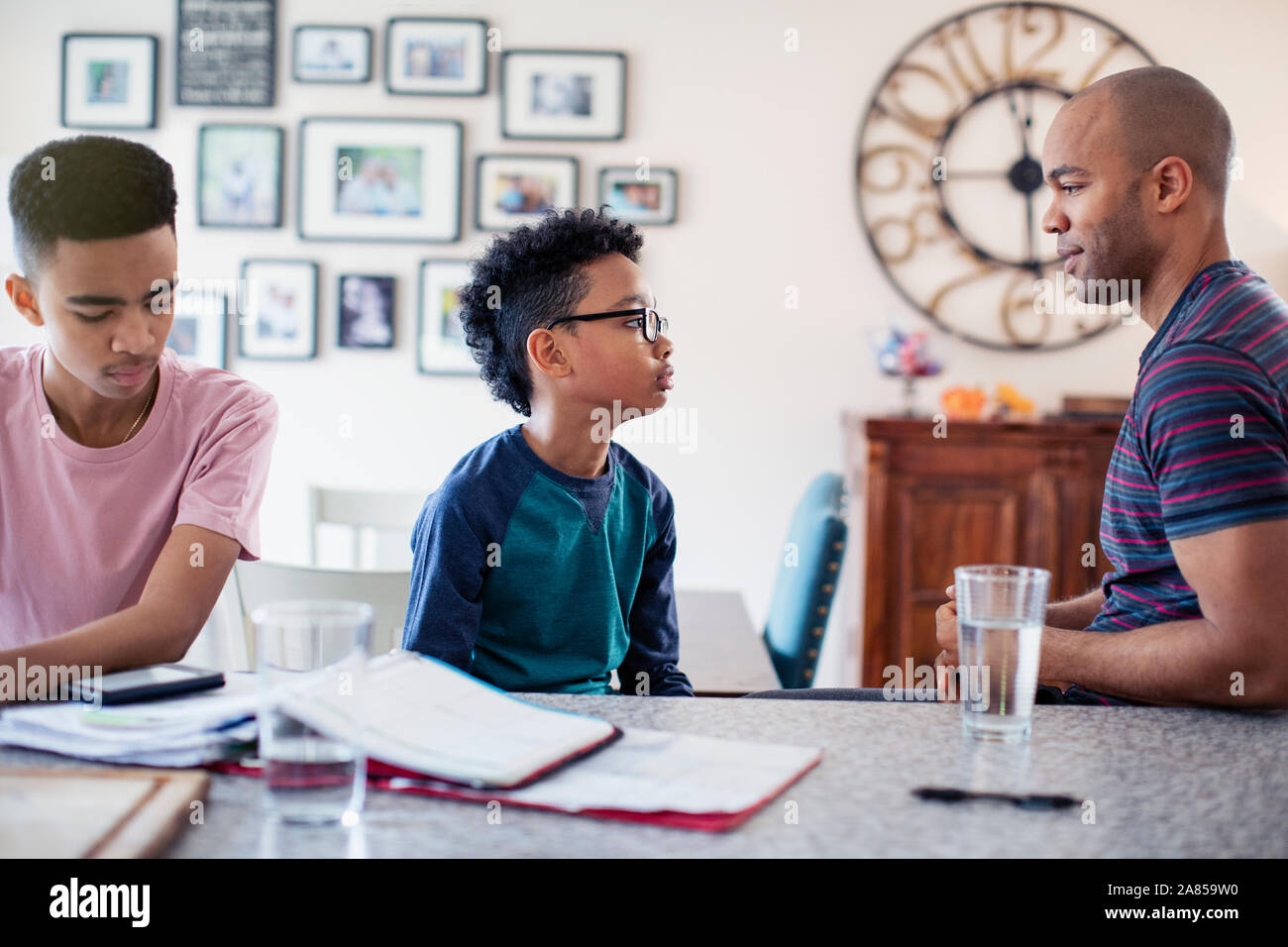 Padre e figli a parlare, facendo i compiti in cucina Foto Stock