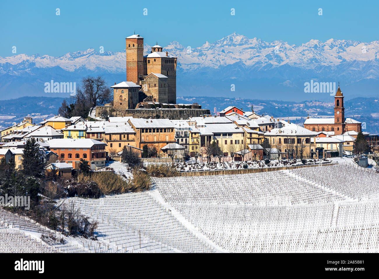 Piccola città medievale e i vigneti in collina innevate come mountain range sullo sfondo in Piemonte, Italia settentrionale. Foto Stock