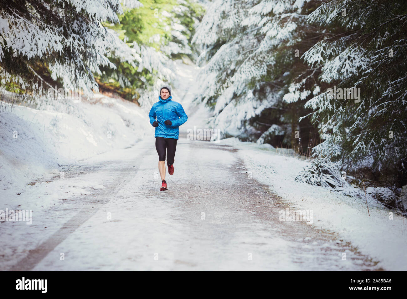 Uomo di jogging sul sentiero nel bosco innevato Foto Stock