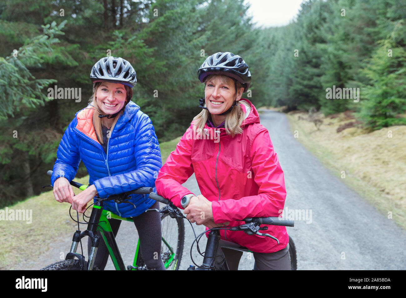 Ritratto felice madre e figlia mountain bike sul sentiero nel bosco Foto Stock