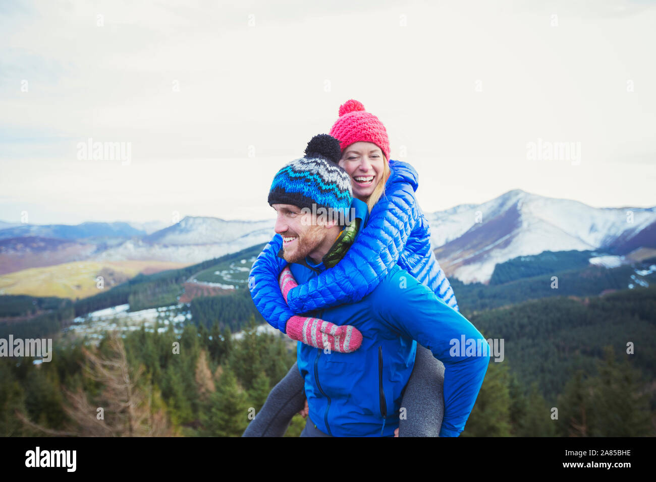 Coppia felice piggybacking con le montagne sullo sfondo, Lake District, REGNO UNITO Foto Stock