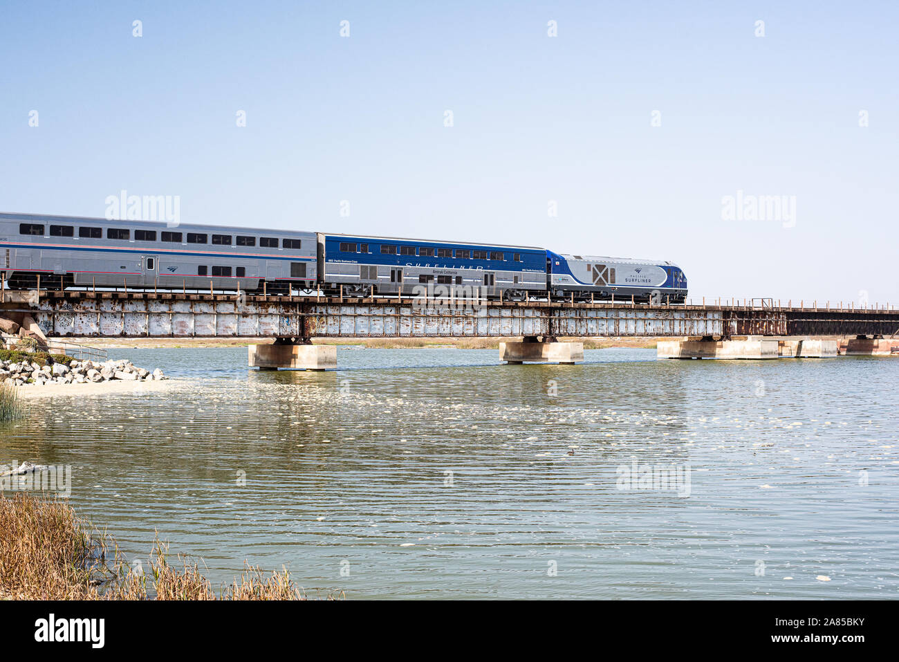 Una visione creativa dei viaggi in California. Un treno Amtrak attraversa una baia, mescolando l'amore dello stato per il viaggio in treno con i suoi paesaggi iconici." Foto Stock