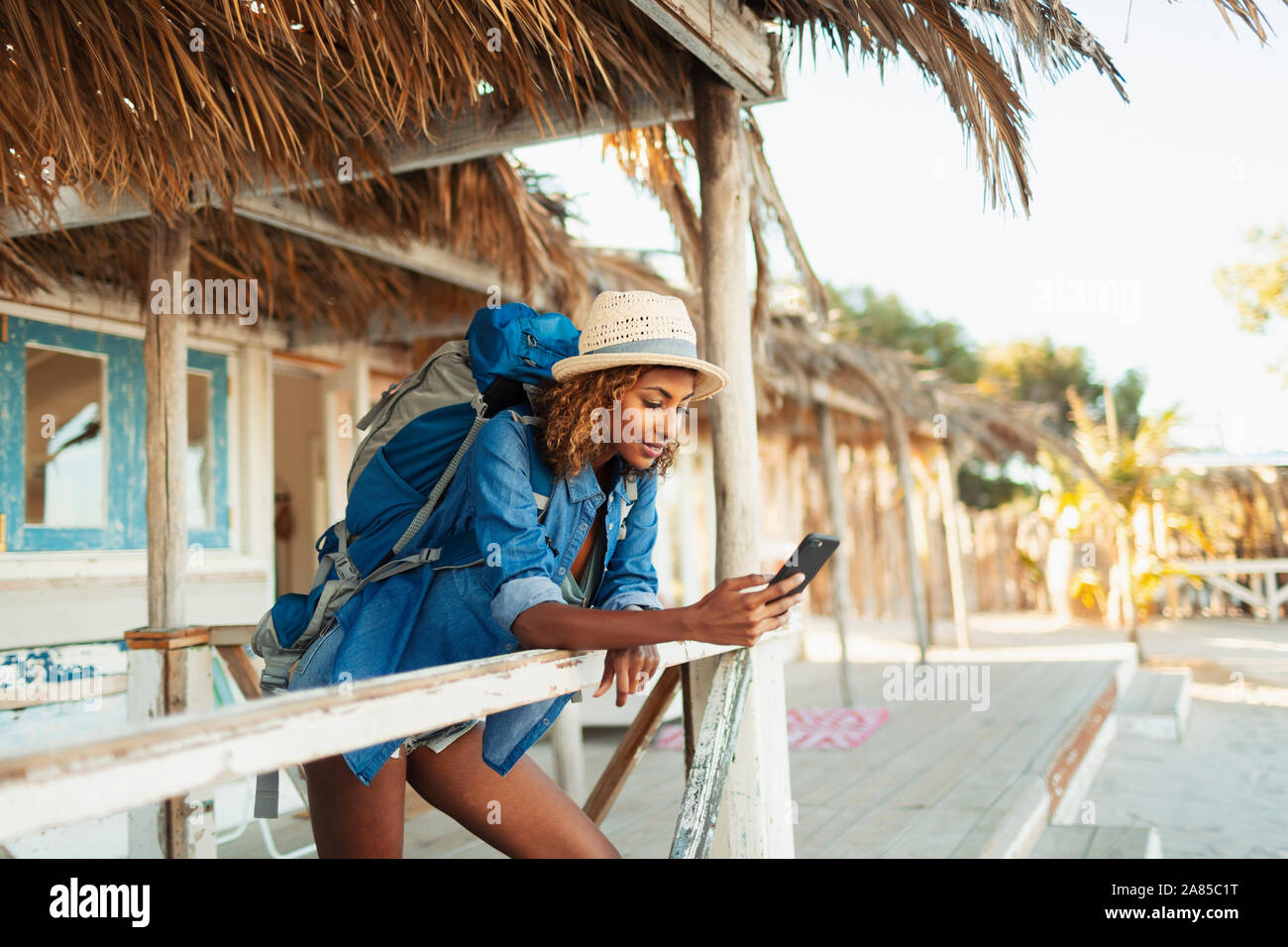 Giovani femmine backpacker utilizzando smart phone su beach hut patio Foto Stock