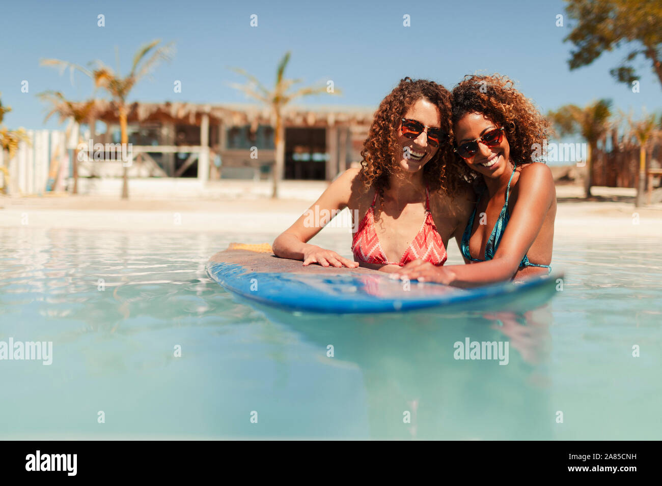 Ritratto felice di donne giovani amici con la tavola da surf nella soleggiata ocean Foto Stock