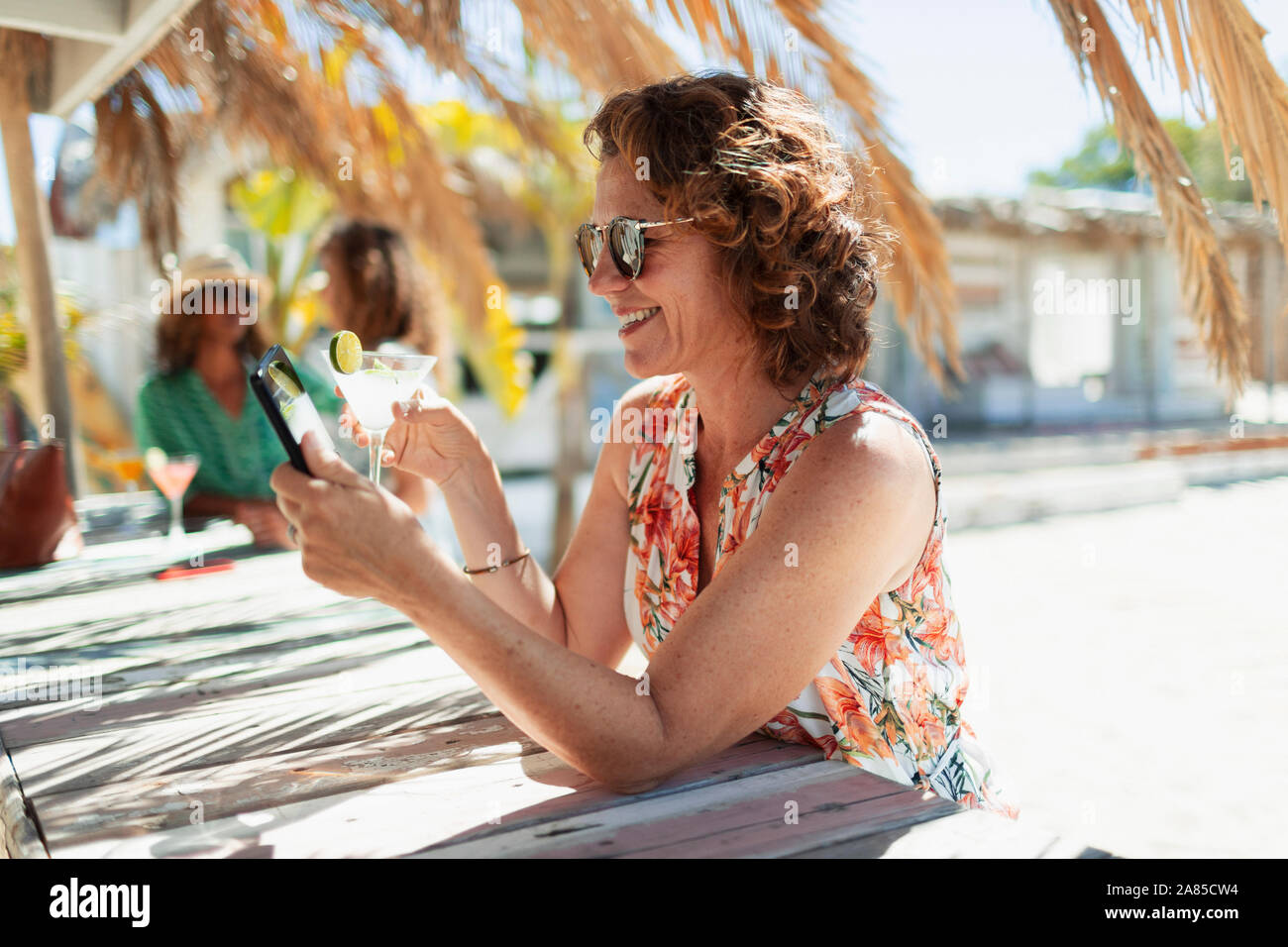 Carefree donna bere cocktail e utilizzo di smart phone a sunny beach bar Foto Stock