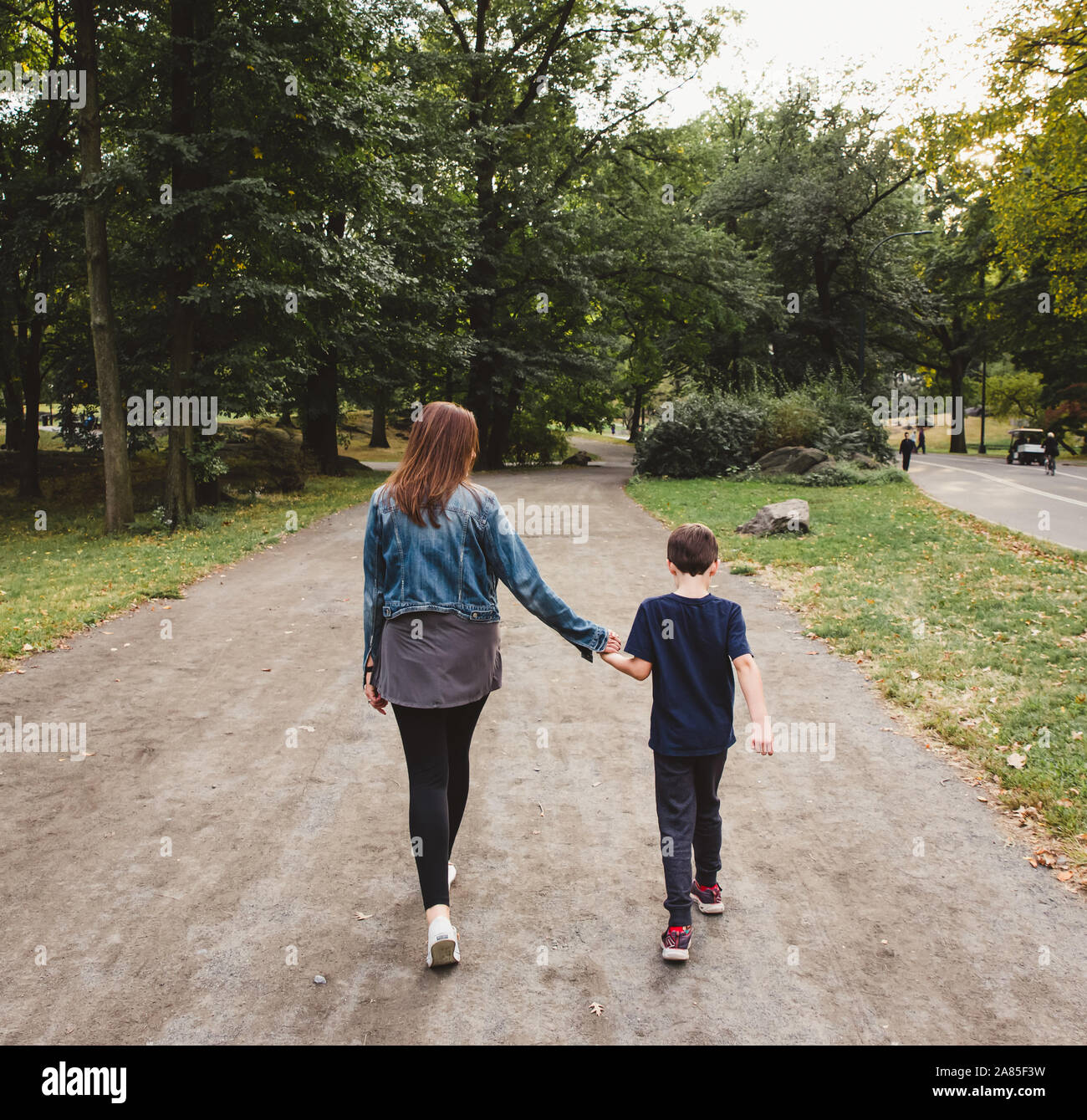 Madre e figlio camminare insieme attraverso un parco colpo da dietro. Foto Stock