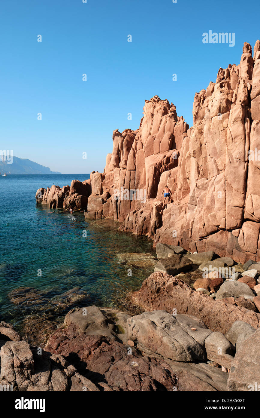 I turisti ad esplorare le rocce rosse / rocce in porfido rosso formazione spiaggia sulla costa della Sardegna ad Arbatax Ogliastra costa di Tortolì, Sardegna, Italia Foto Stock