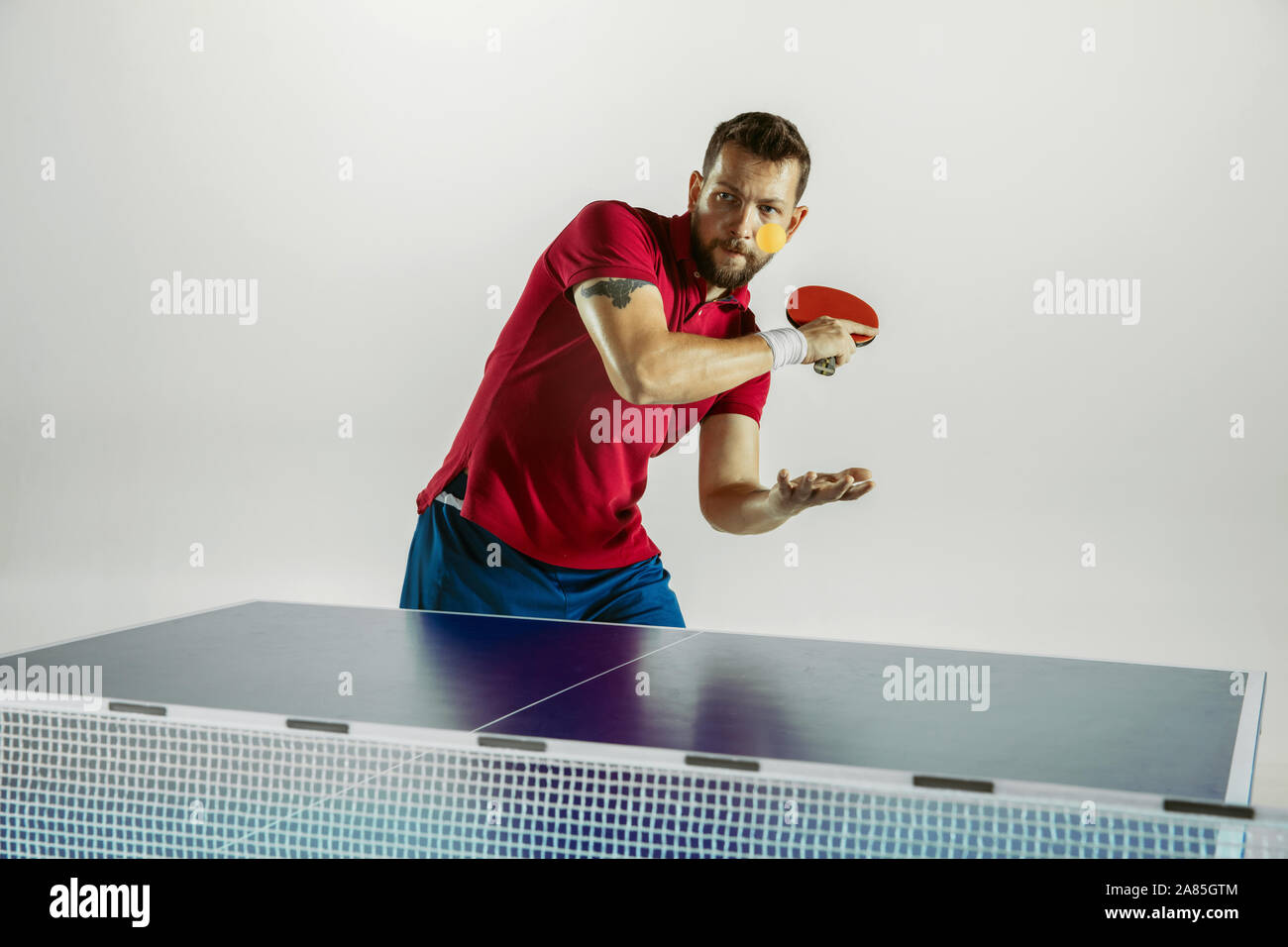 Lotta. Giovane uomo gioca ping pong su bianco di sfondo per studio. Il modello riproduce il ping pong. Concetto di attività per il tempo libero, lo sport, le emozioni umane nel gioco, uno stile di vita sano, motion, azione, movimento. Foto Stock