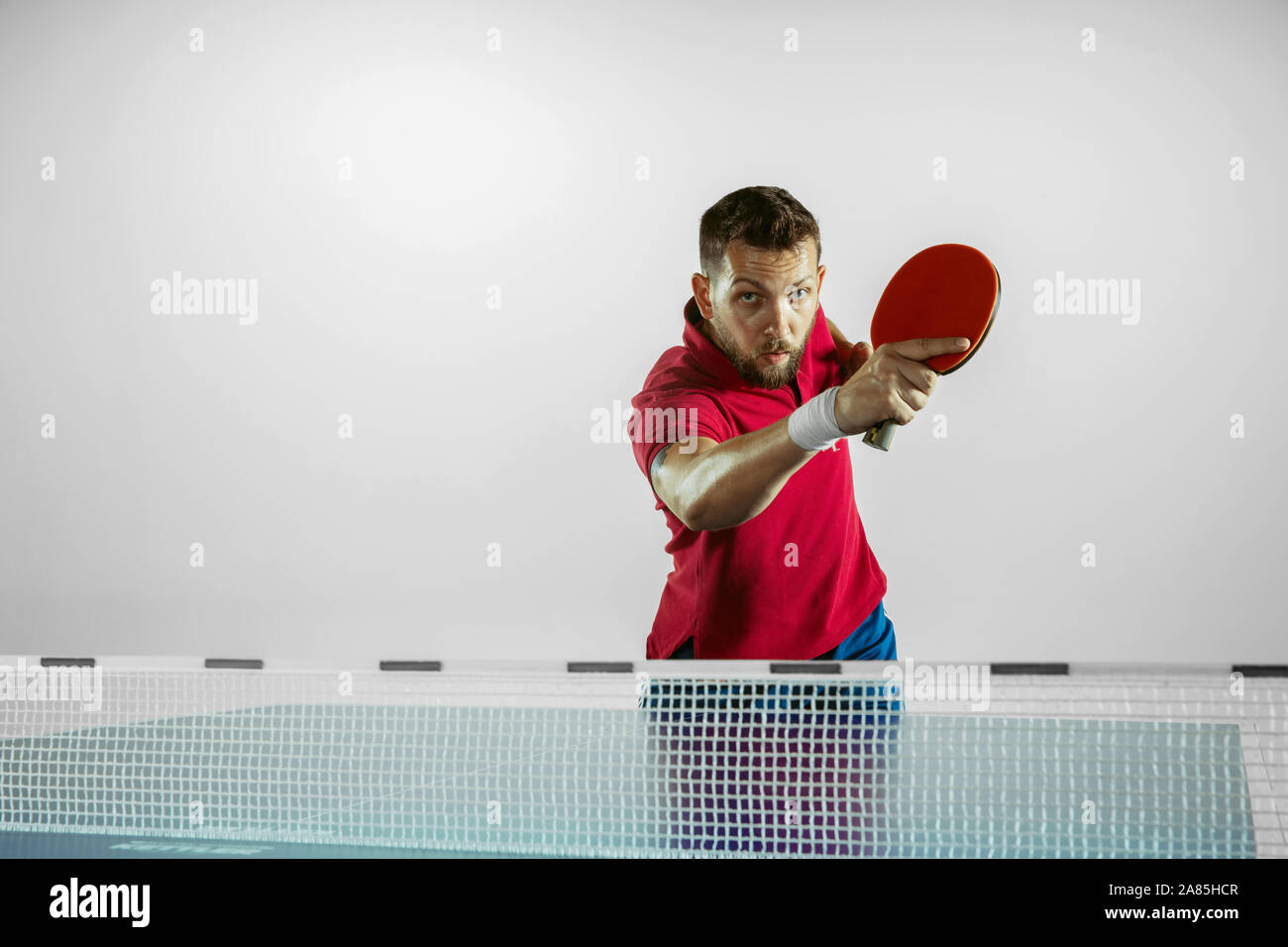 In questo momento. Giovane uomo gioca ping pong su bianco di sfondo per studio. Il modello riproduce il ping pong. Concetto di attività per il tempo libero, lo sport, le emozioni umane nel gioco, uno stile di vita sano, motion, azione, movimento. Foto Stock