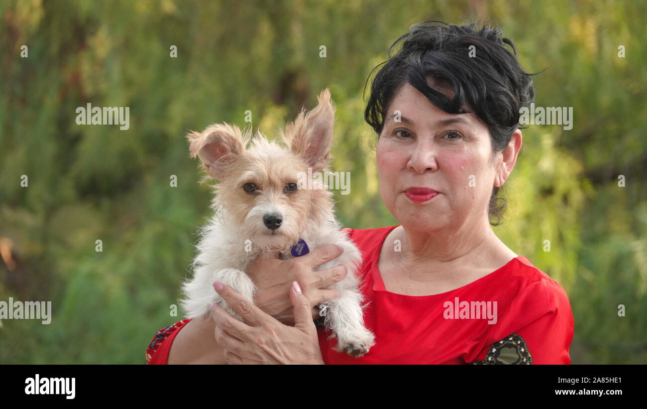 Senior ispanica donna nella sua 60's tenendo il suo simpatico cagnolino Foto Stock