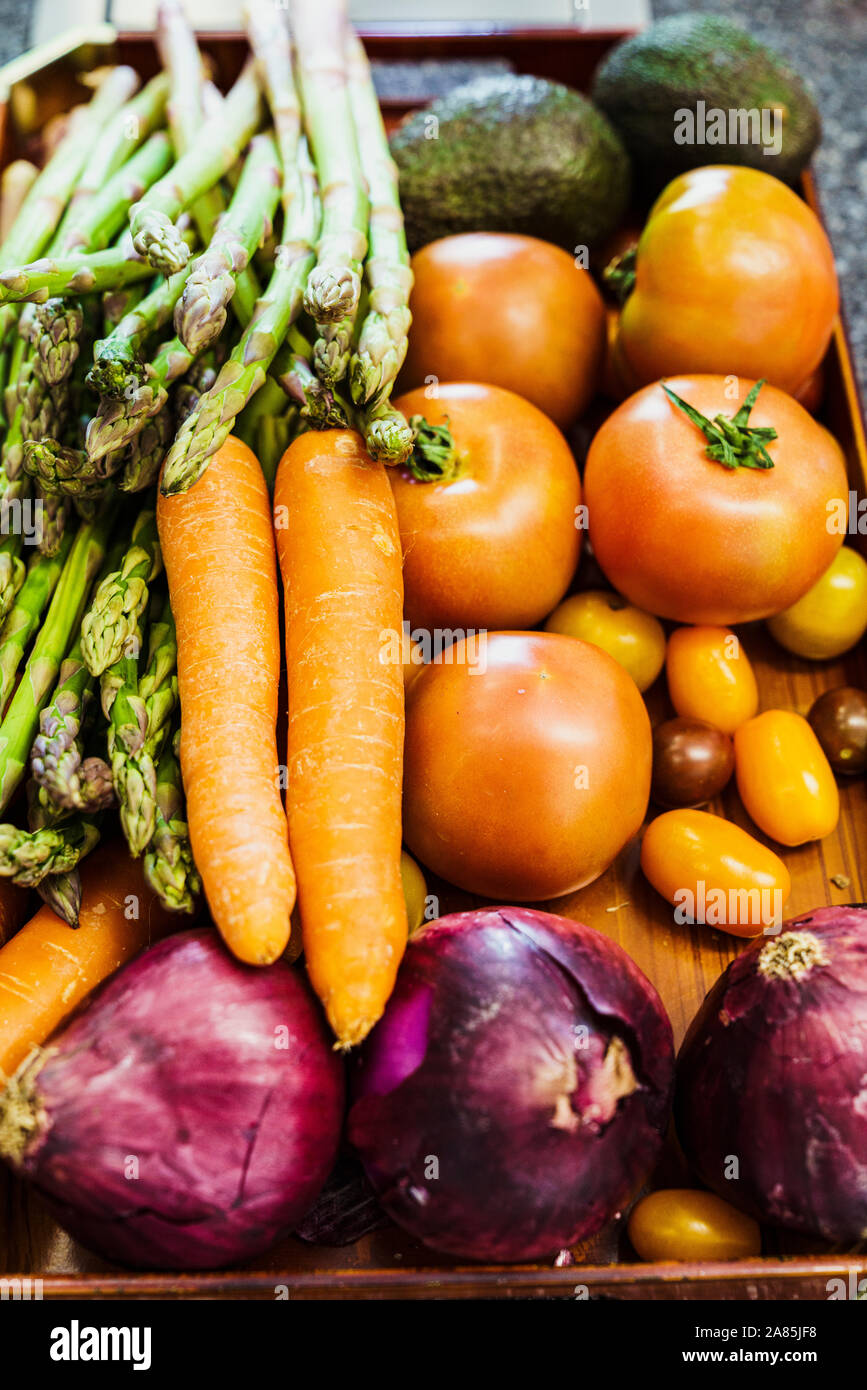 Stock Foto di una scatola di legno con pomodori, carote, avocadi, gli asparagi e le cipolle. Foto verticale e di condurre una vita sana nozione Foto Stock