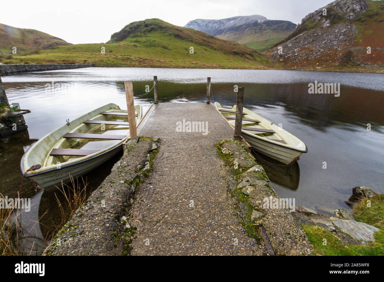 Due barche e jetty, sul tranquillo lago. Llyn y Dywarchen, Rhyd Ddu, Snowdonia, il Galles del Nord, Gwynedd, paesaggio Foto Stock