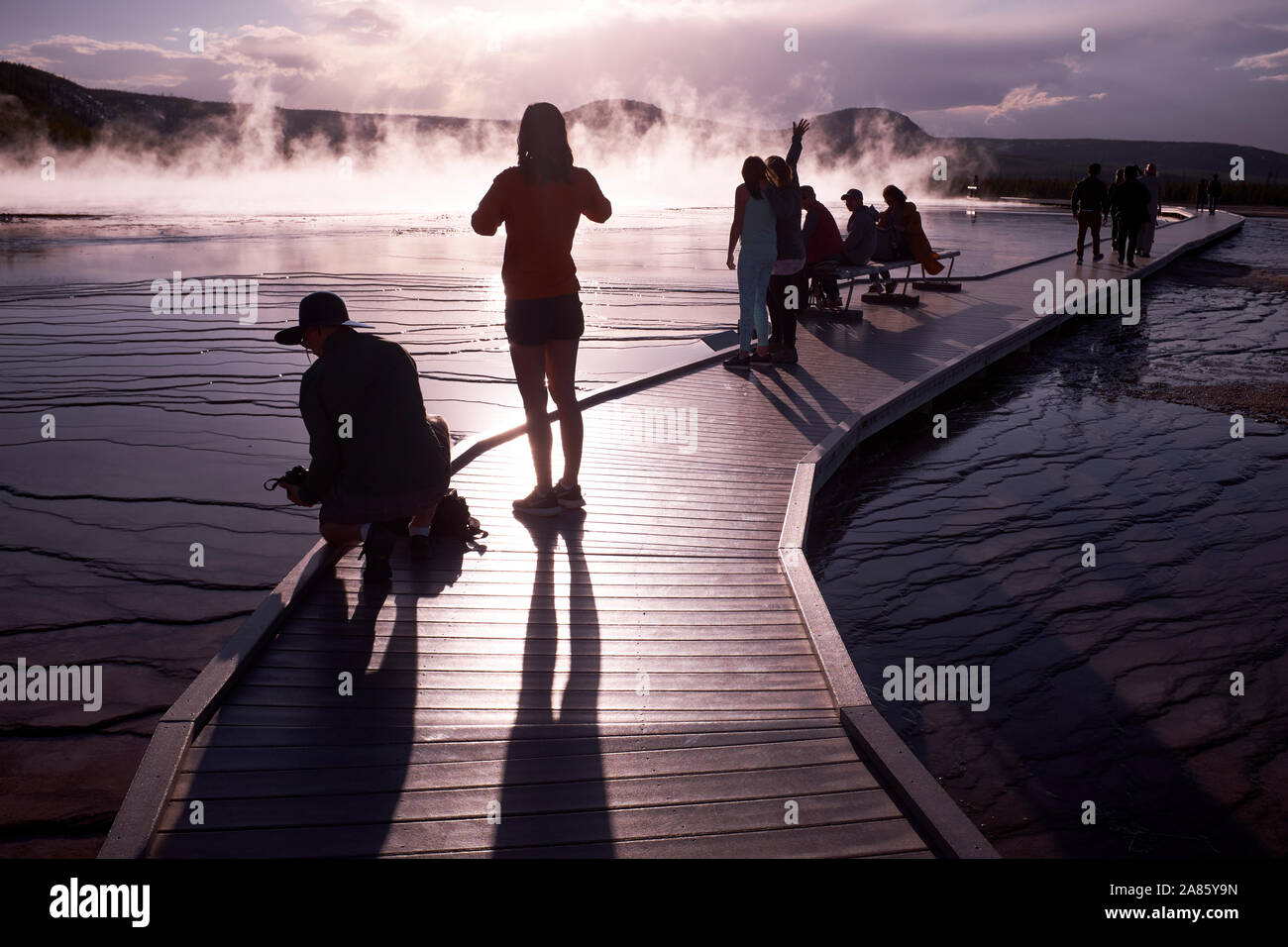 I visitatori si stagliano contro il sole e la crescita del vapore a Grand Prismatic Hot Springs nel Parco Nazionale di Yellowstone, Wyoming USA Foto Stock