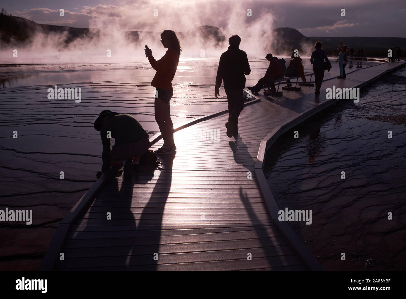 I visitatori si stagliano contro il sole e la crescita del vapore a Grand Prismatic Hot Springs nel Parco Nazionale di Yellowstone, Wyoming USA Foto Stock