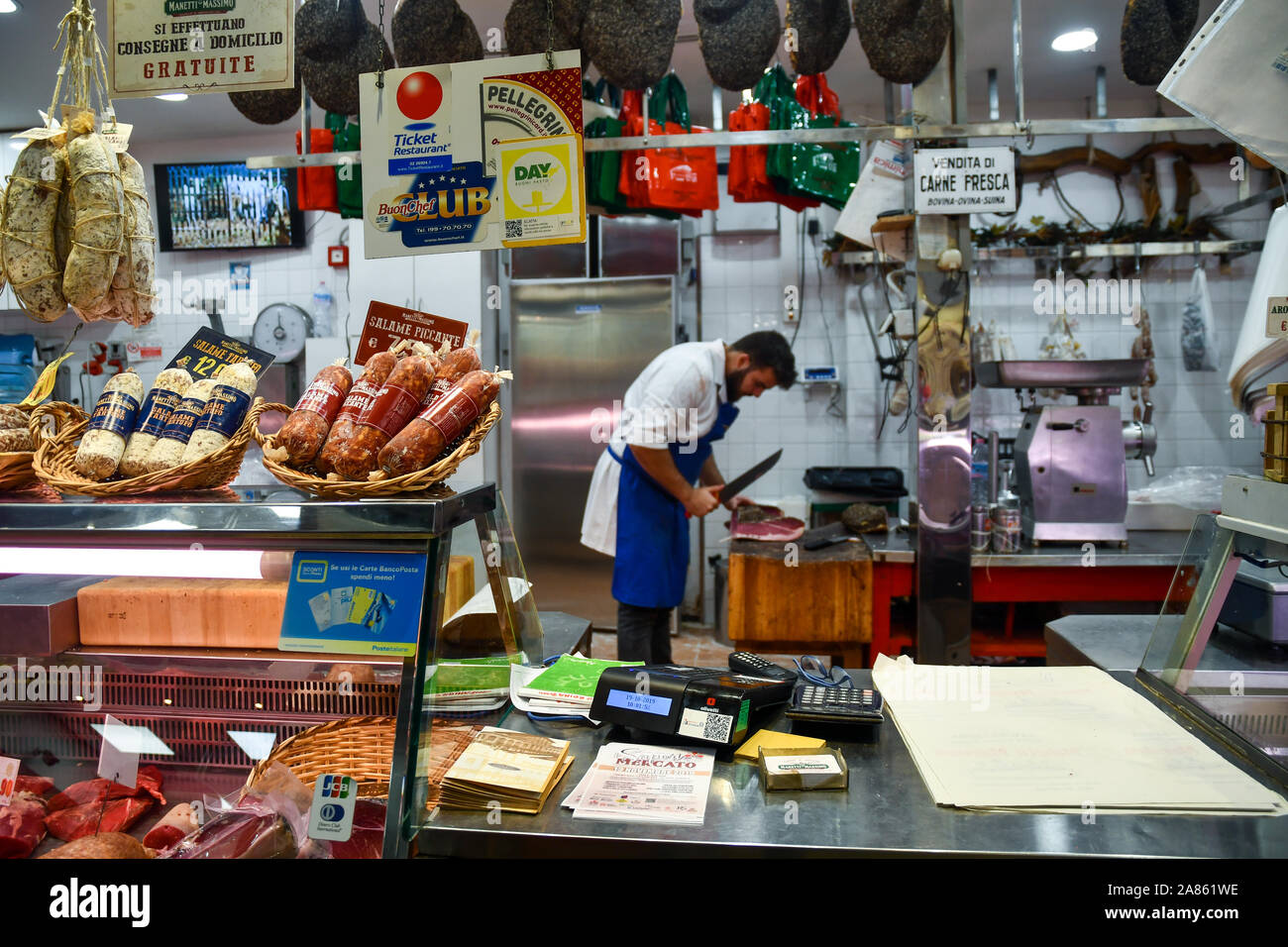 Contatore di una macelleria all'interno del Mercato Centrale di San Lorenzo con un macellaio il taglio di un prosciutto in background, Firenze, Toscana, Italia Foto Stock