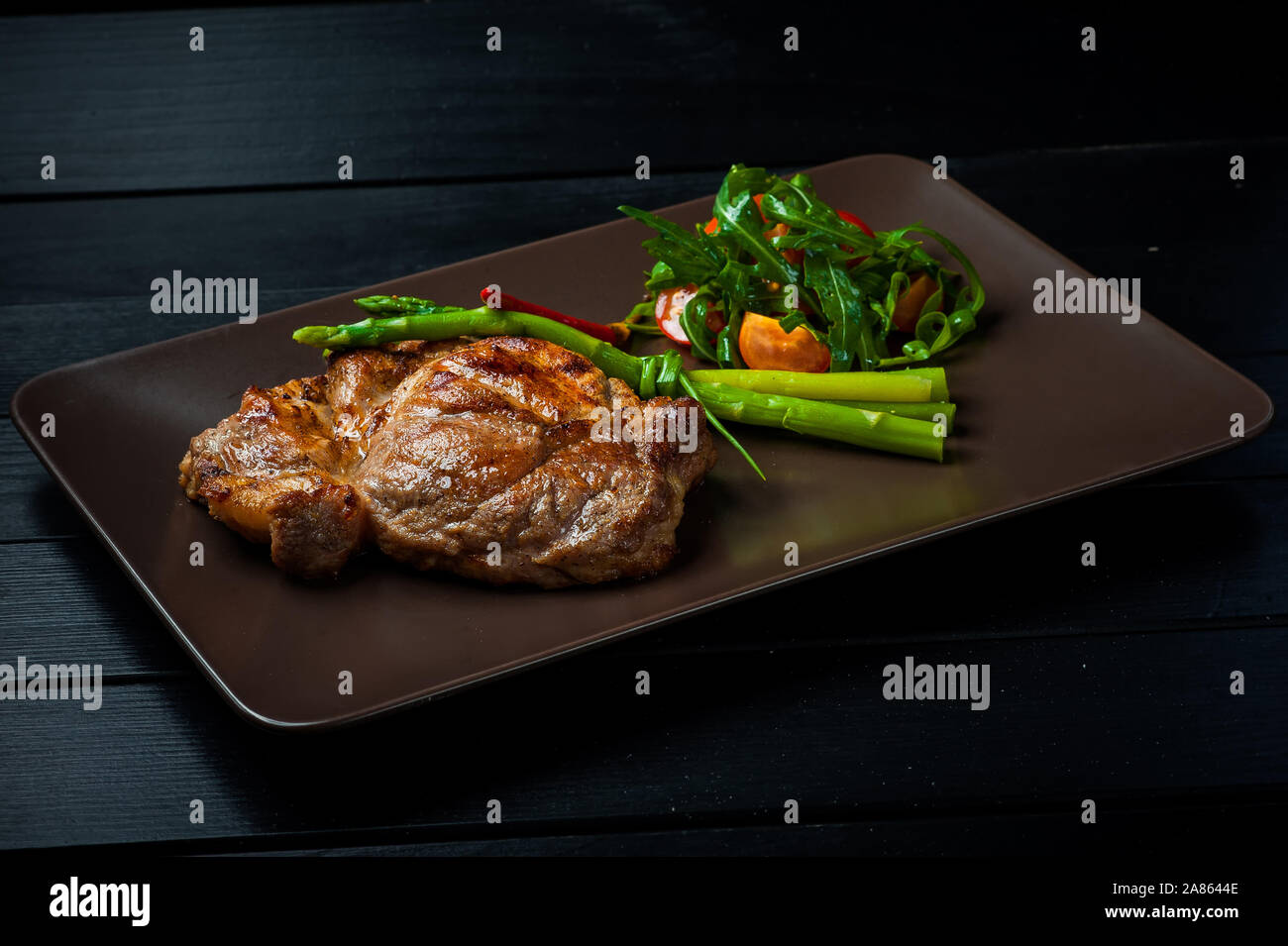 Una bella succosa bistecca con insalata su un rettilineo marrone a piastra è sul tavolo. Foto Stock