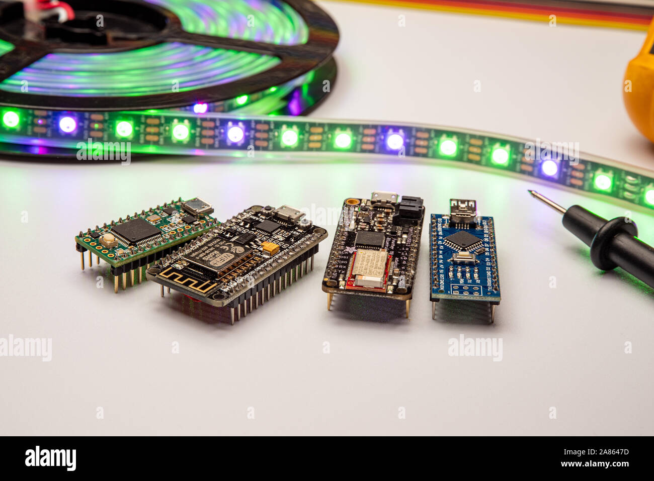Selezione di piccole schede di sviluppo visualizzata con una striscia di LED, il metro e il ponticello dello sfondo. Schede madri includono minuscolo, piume, esp8266 e nano. Foto Stock