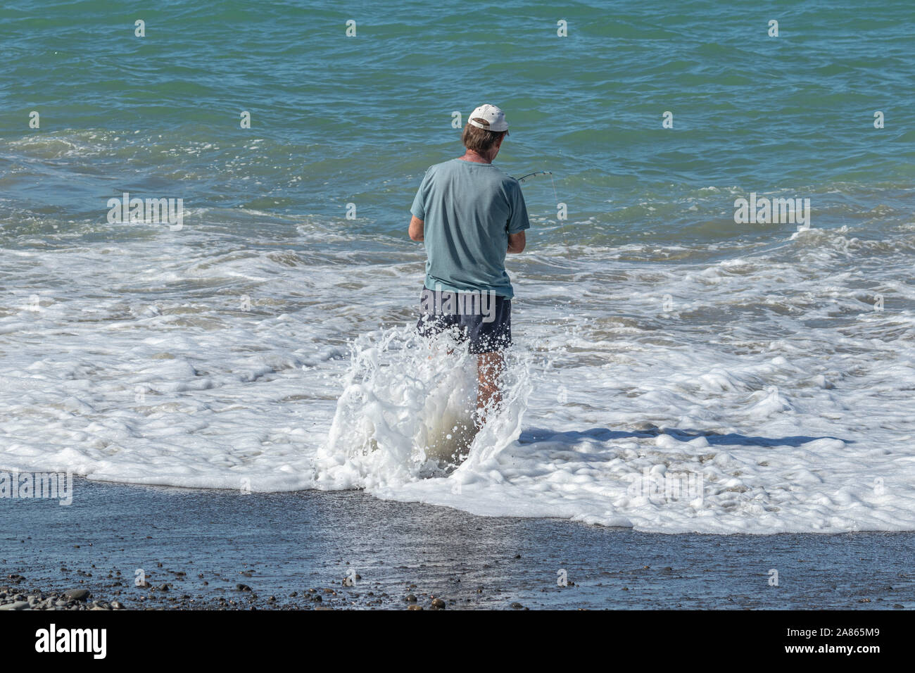 Uomo in piedi in surf con la pesca road Foto Stock