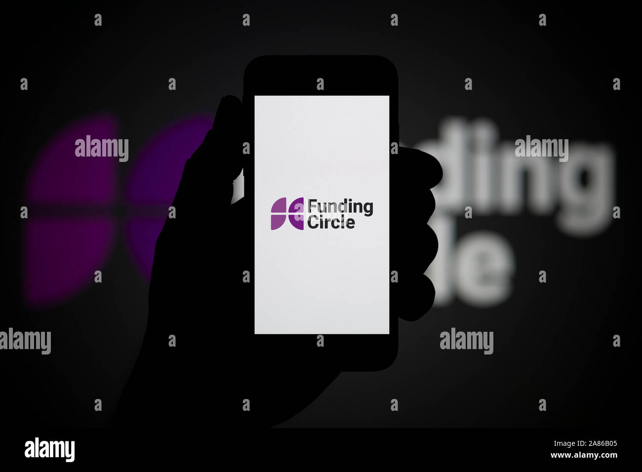 Un uomo guarda al suo iPhone che visualizza il finanziamento del logo a forma di cerchio, con lo stesso logo in background (solo uso editoriale). Foto Stock