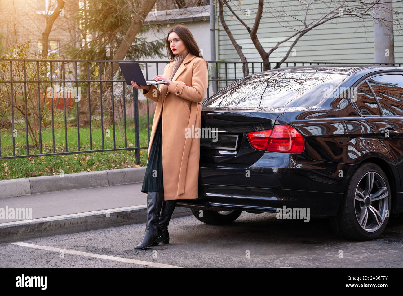 Donna con notebook appoggiato contro la sua automobile Foto Stock