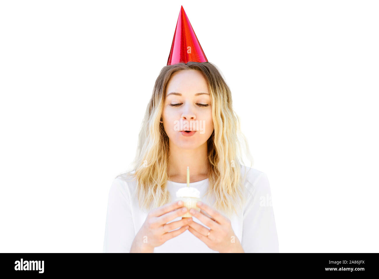 Giovane donna con cappello di partito e compleanno cupcake brucia le sue candele Foto Stock