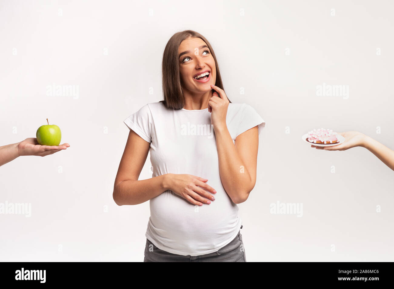 Donna incinta scegliendo tra Apple e la ciambella in piedi, Studio Shot Foto Stock