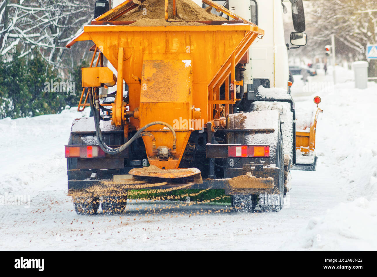 Auto comunale spruzza strade innevate con sabbia e sale. Lo spalaneve. Inverno anti-slittamento su strada il concetto di manipolazione Foto Stock