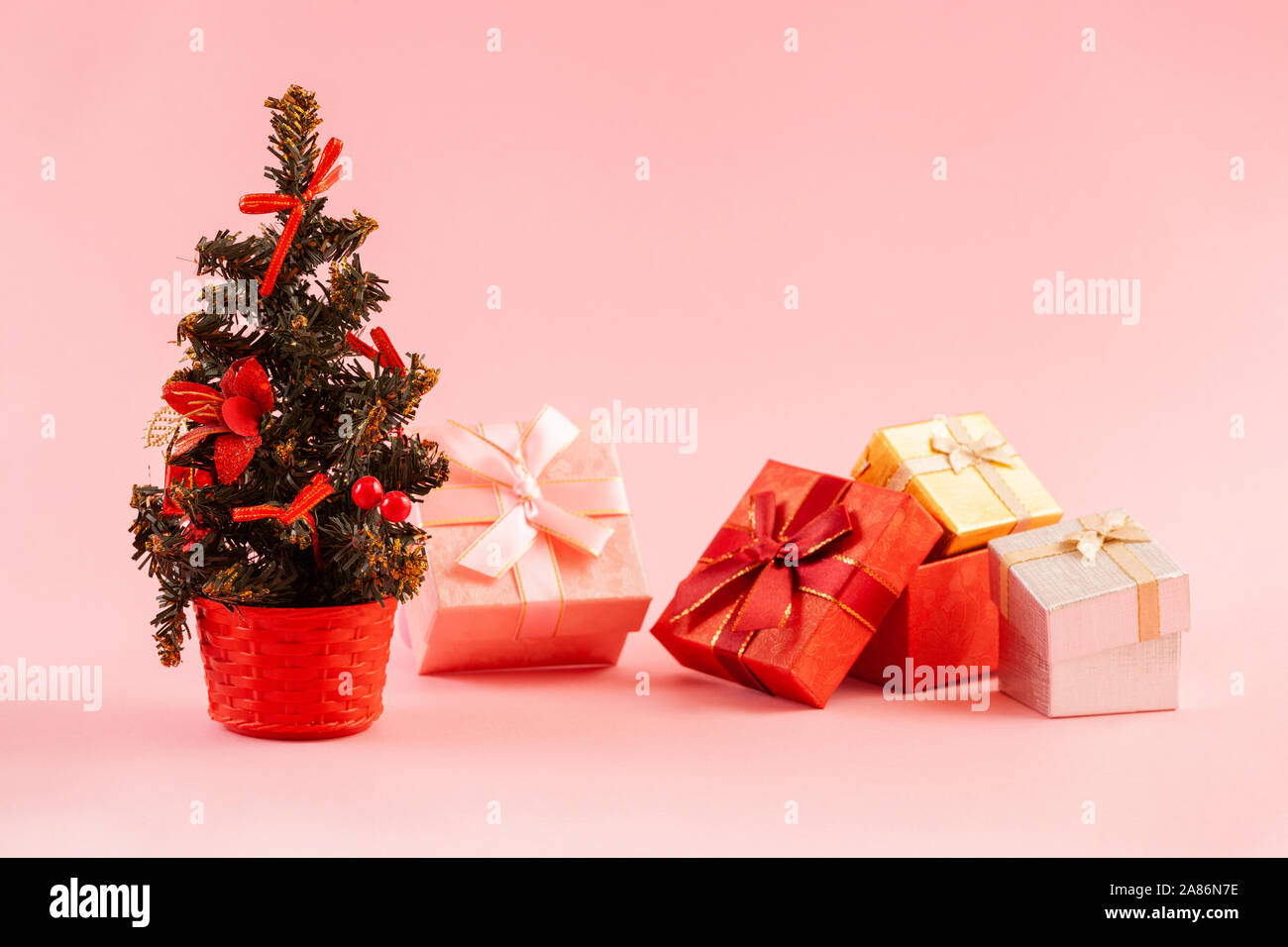 Concetto di natale. Albero di Natale decorato con quattro scatole regalo su uno sfondo di colore rosa. Foto Stock