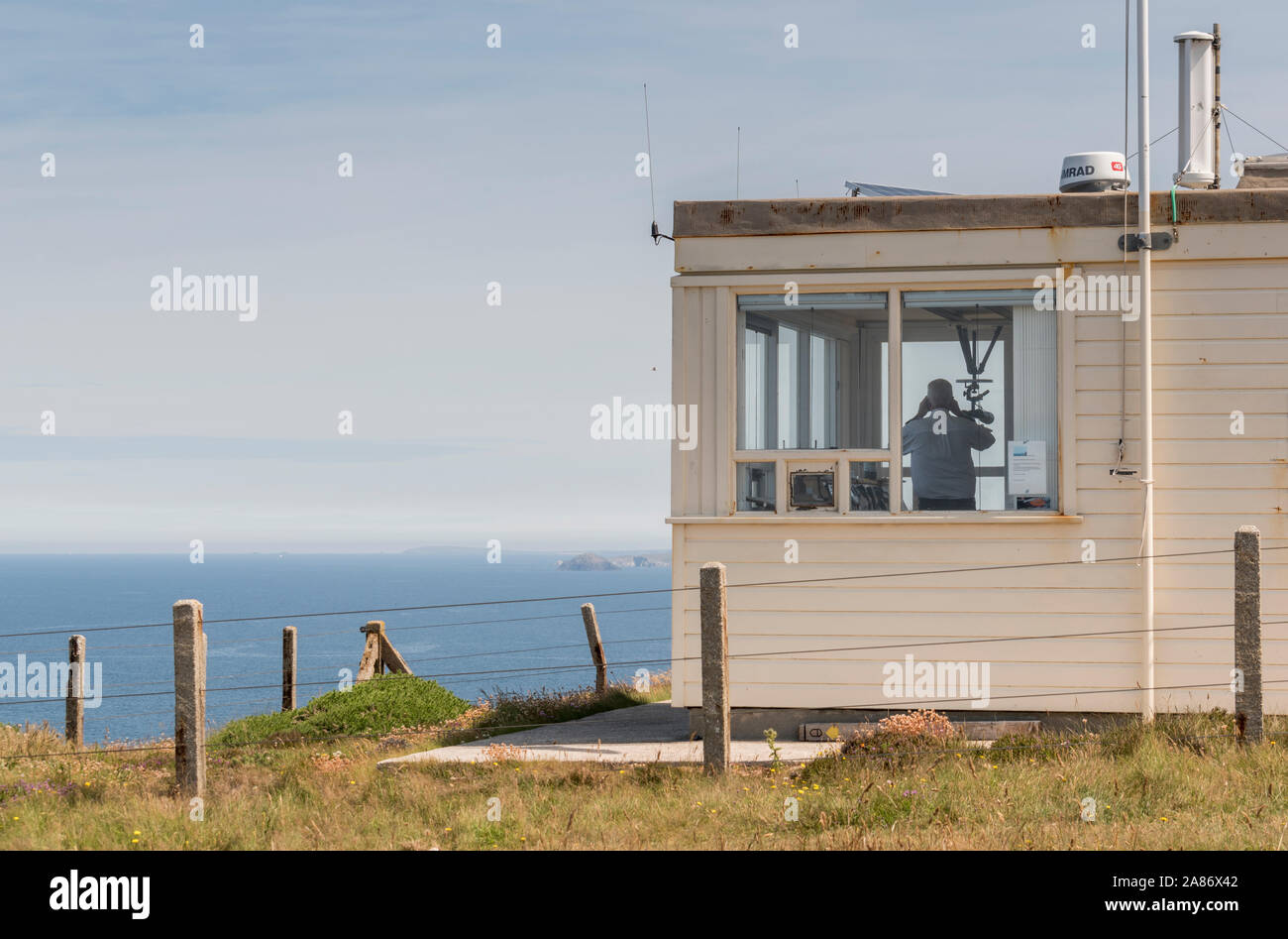 Un Watchkeeper usando il suo binocolo a guardare lungo la costa a St Agnes dalla NSC watchpower Foto Stock