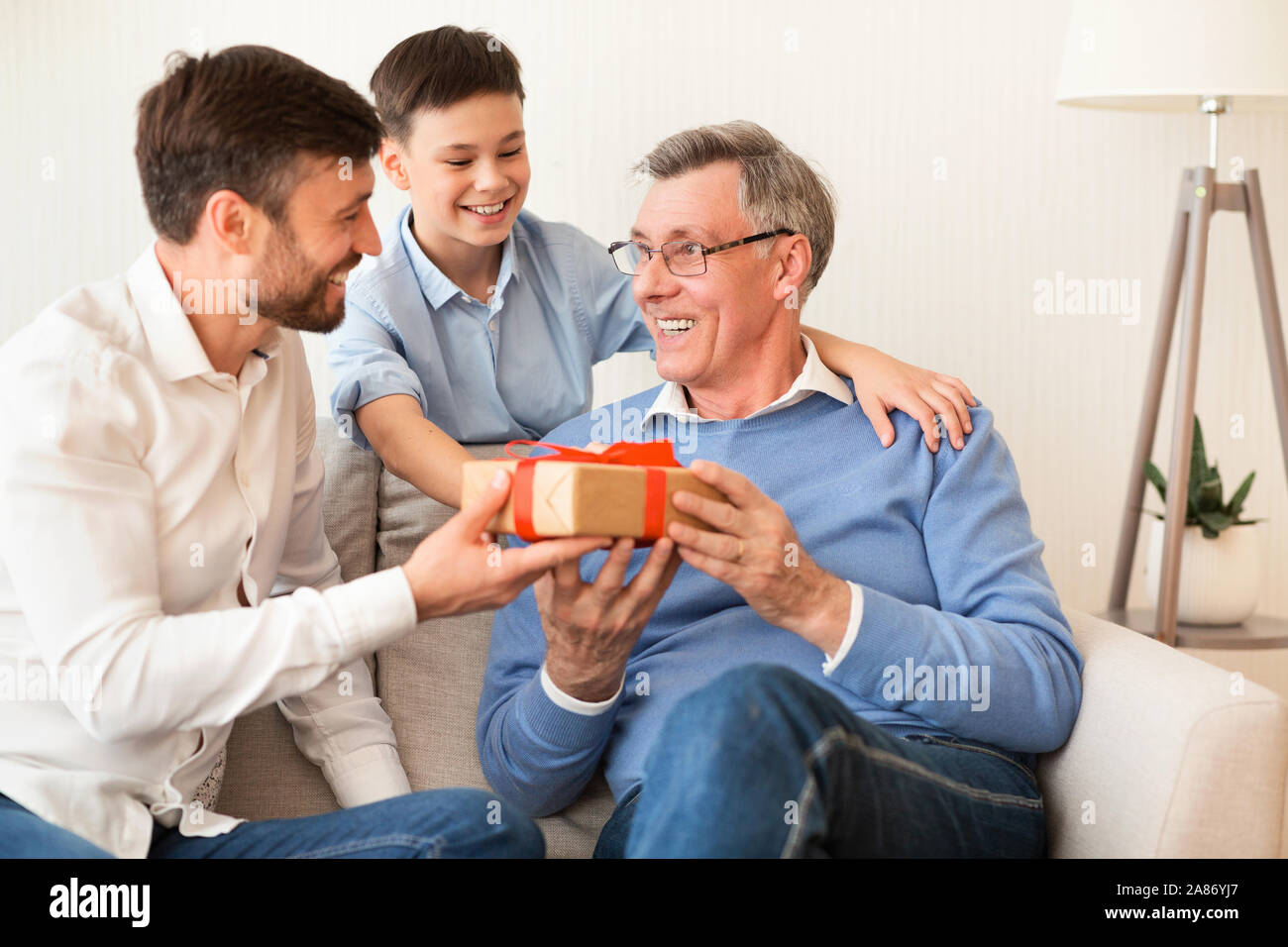 Padre e Figlio congratulandosi con il nonno dando regalo di compleanno a casa Foto Stock
