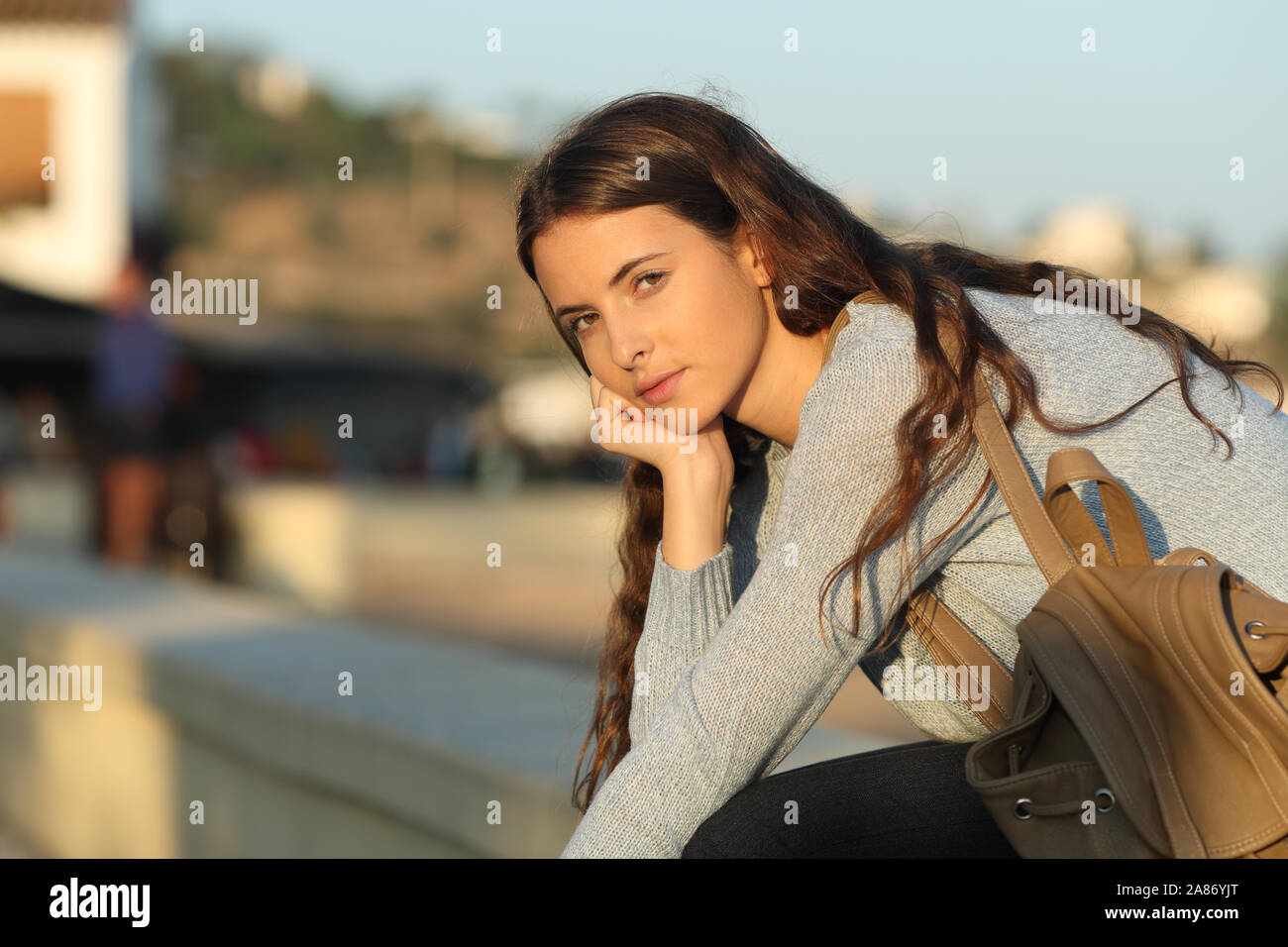 Grave ragazza casual ti guarda al tramonto seduti in strada Foto Stock