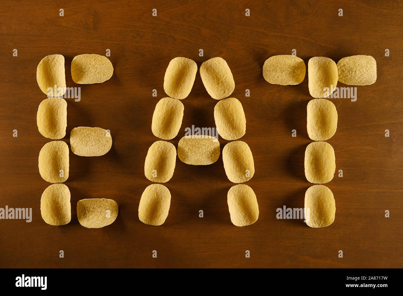 Potato Chips su una tavola di legno, lo sfondo con il testo "mangiare", concetto di design sul tema del fast food e malsano, dieta e aumento del rischio di obesità Foto Stock