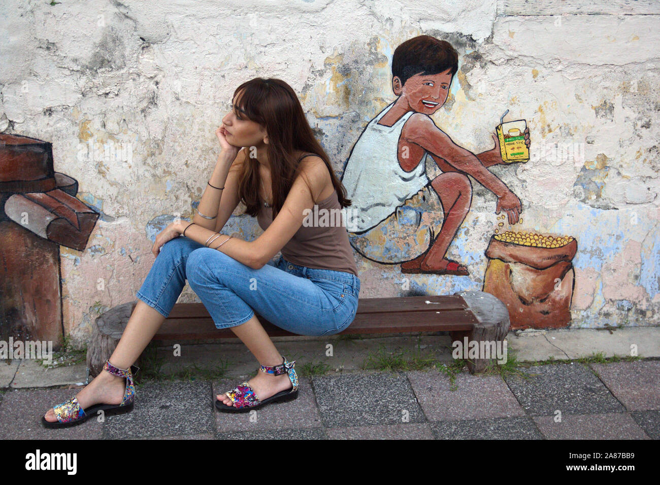 Una giovane donna pone contro un murale in una strada di Ipoh, Perak, Malaysia Foto Stock